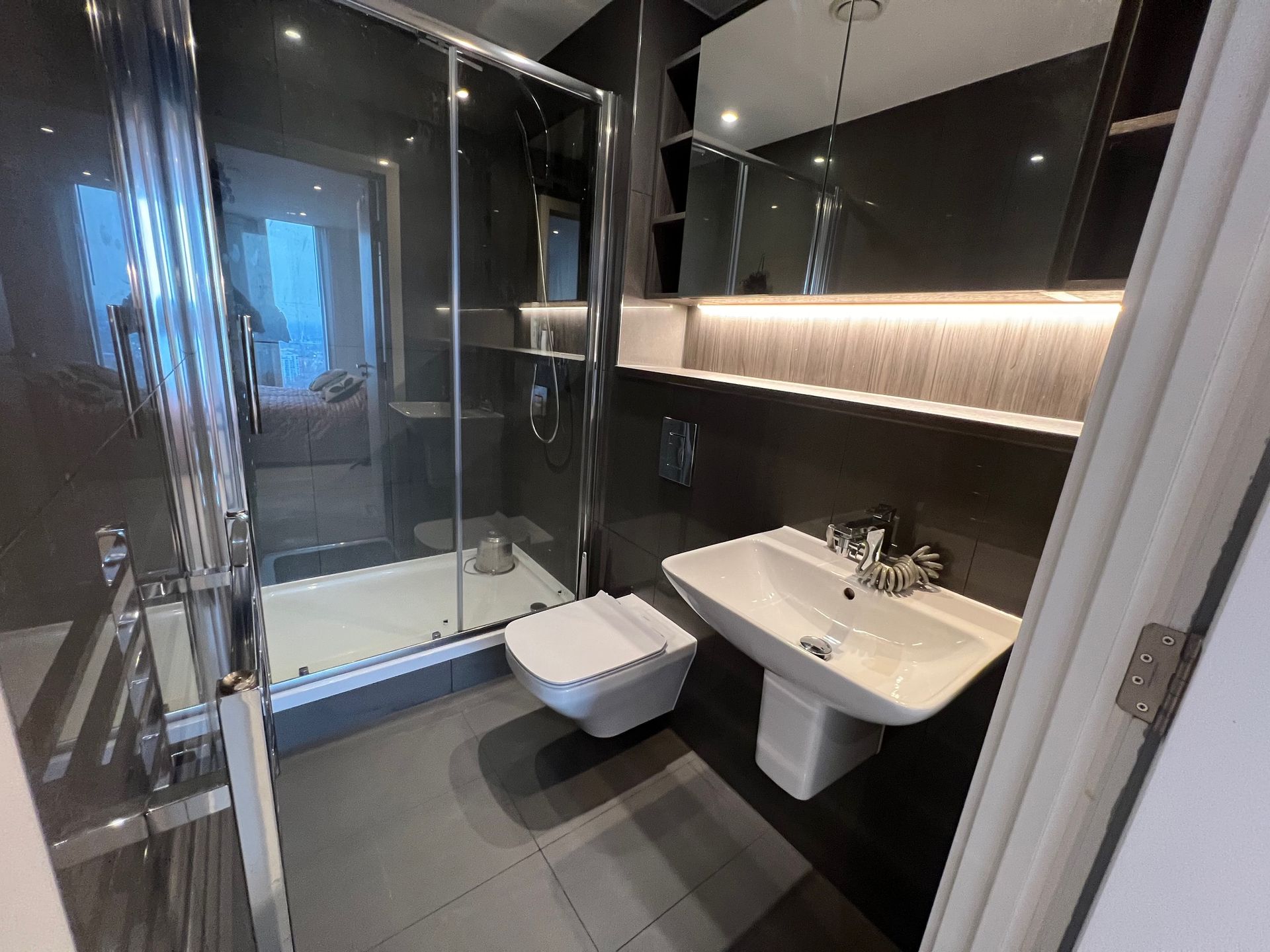Modern bathroom with gray tiles, a glass shower, toilet, and sink.