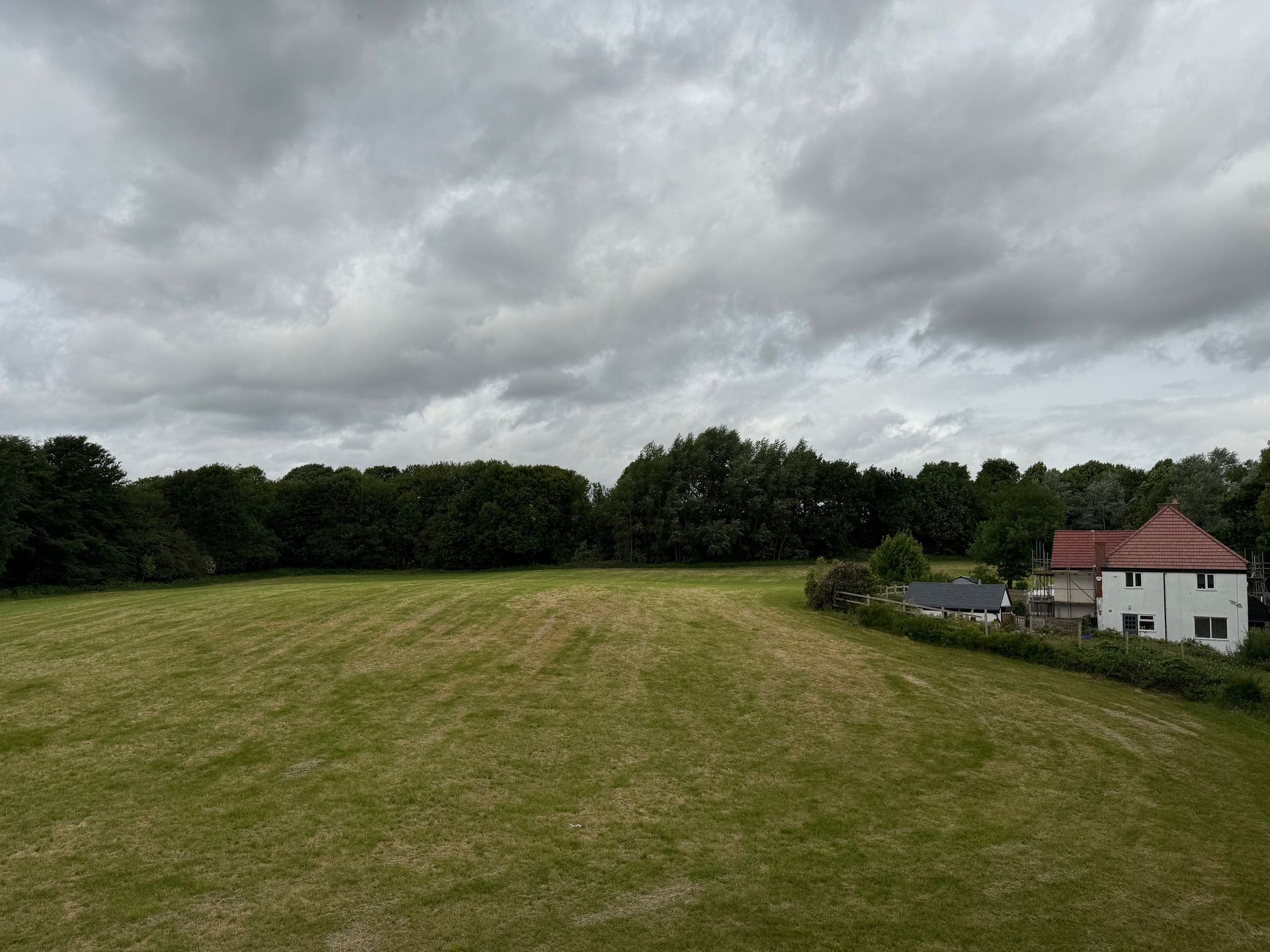 Overcast sky over a grassy field, bordered by trees and a house.