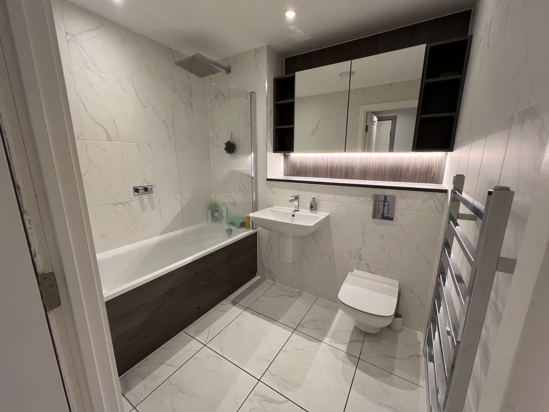 Modern bathroom with bathtub, toilet, sink, and mirrored cabinet. White and gray tones.