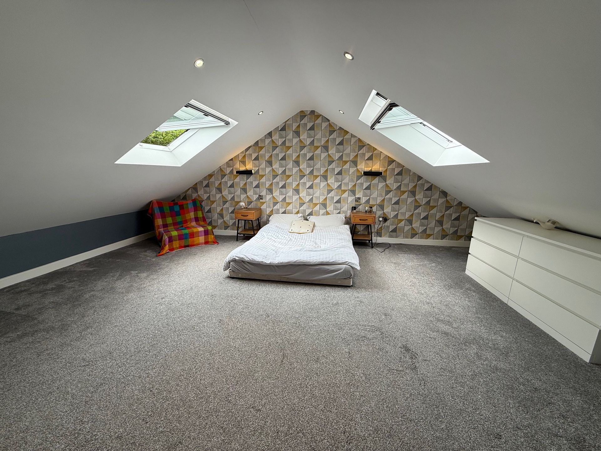 Loft bedroom with bed, two skylights, patterned wallpaper, and gray carpet.