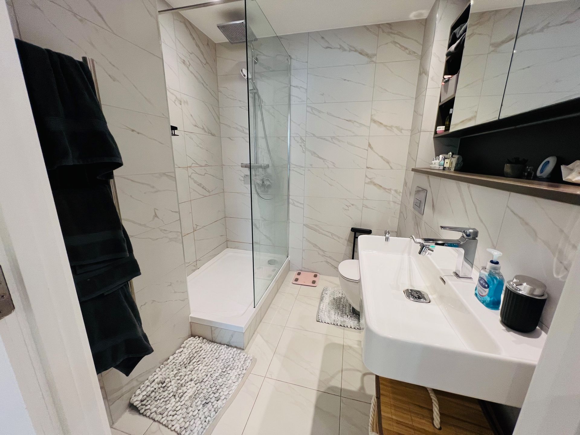 Bathroom with white marble tiles, shower, sink, and dark towel rack.