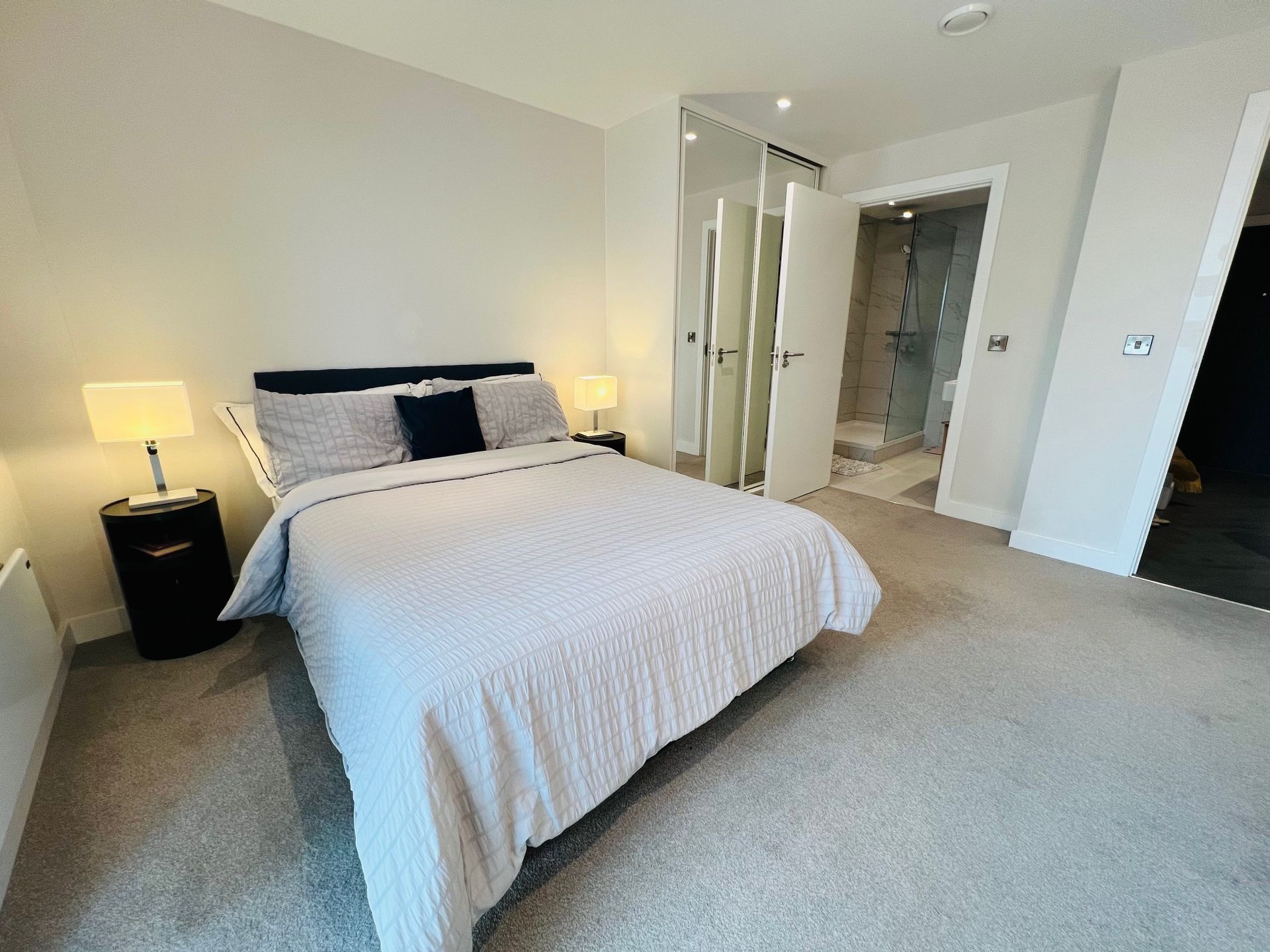 Bedroom with bed, nightstands, and en-suite bathroom. Light gray walls, carpet, and bedding.