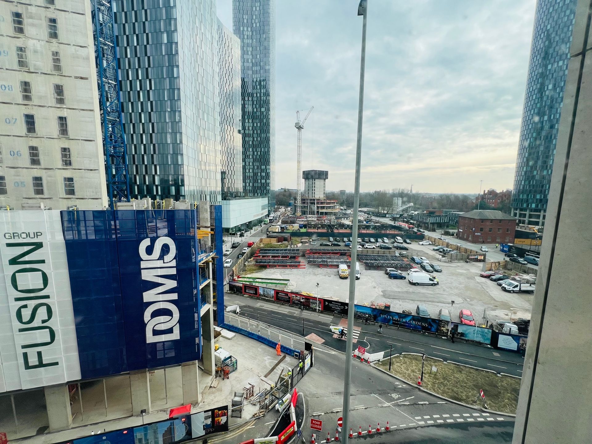 Construction site with tall buildings, cranes, and a road. Blue and white colors dominate.