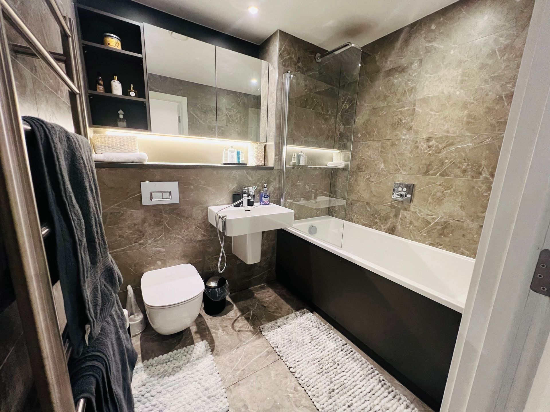 Modern bathroom with gray tile, toilet, sink, tub, and towel warmer.
