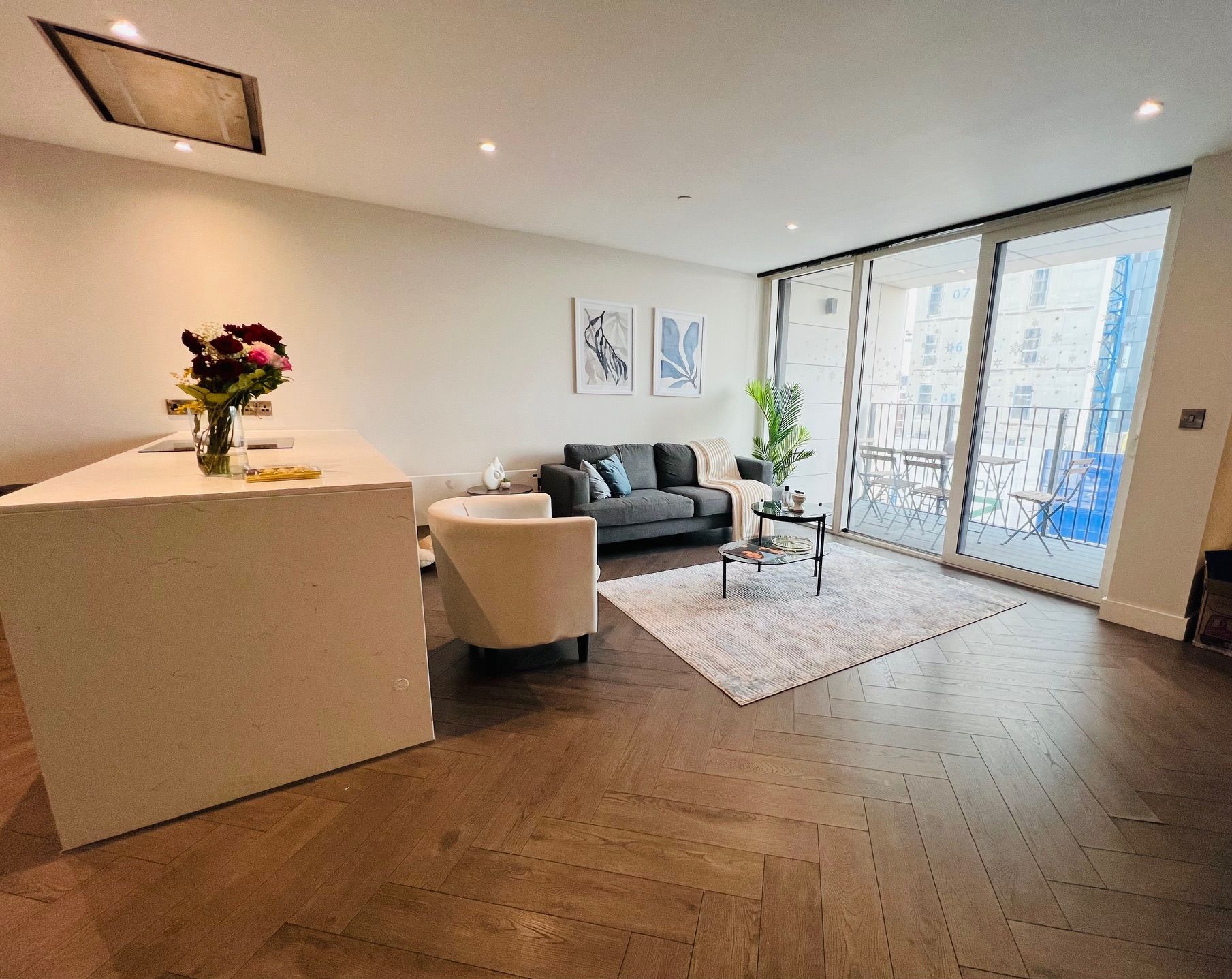 Modern living room with open layout, including a kitchen island, sofa, and balcony access.