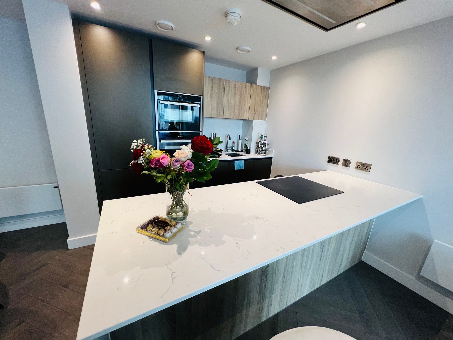 Modern kitchen with a white countertop island, built-in appliances, and a vase of flowers.