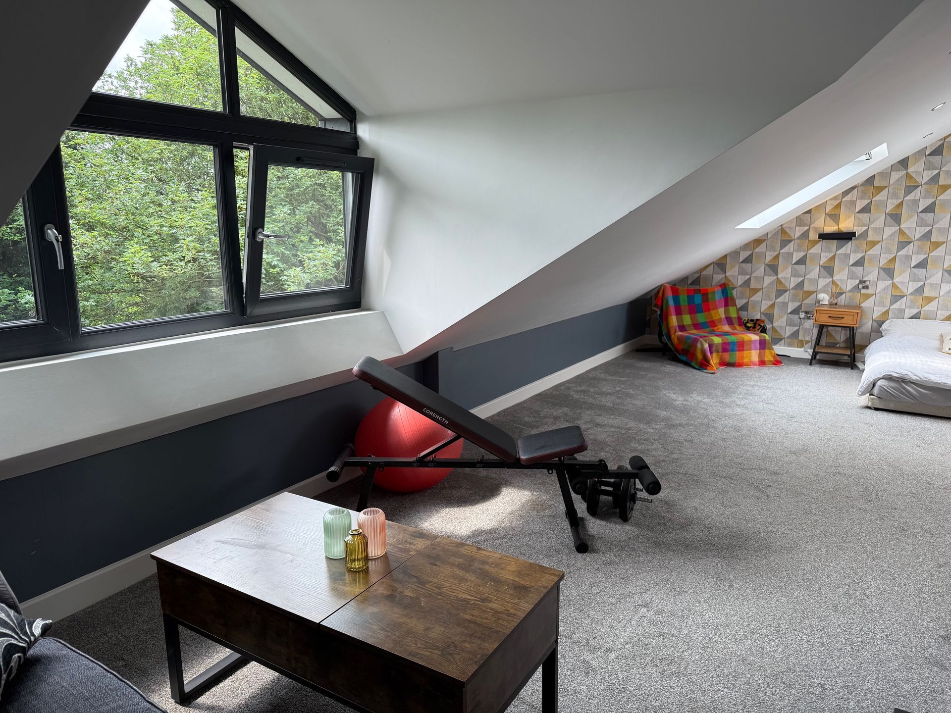 Gym with angled walls, window, exercise bench, red ball, and patterned wallpaper.
