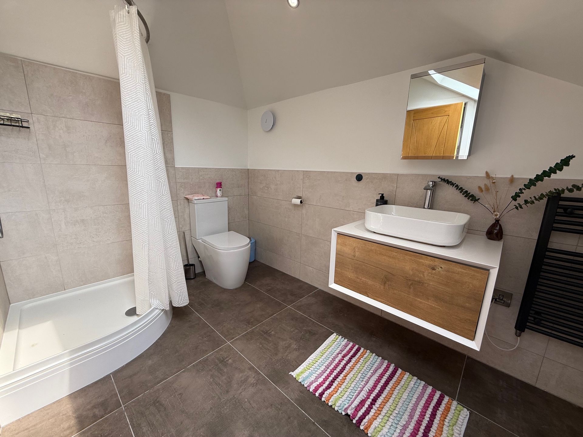 Bathroom with shower, toilet, floating sink vanity, mirror, and colorful rug.