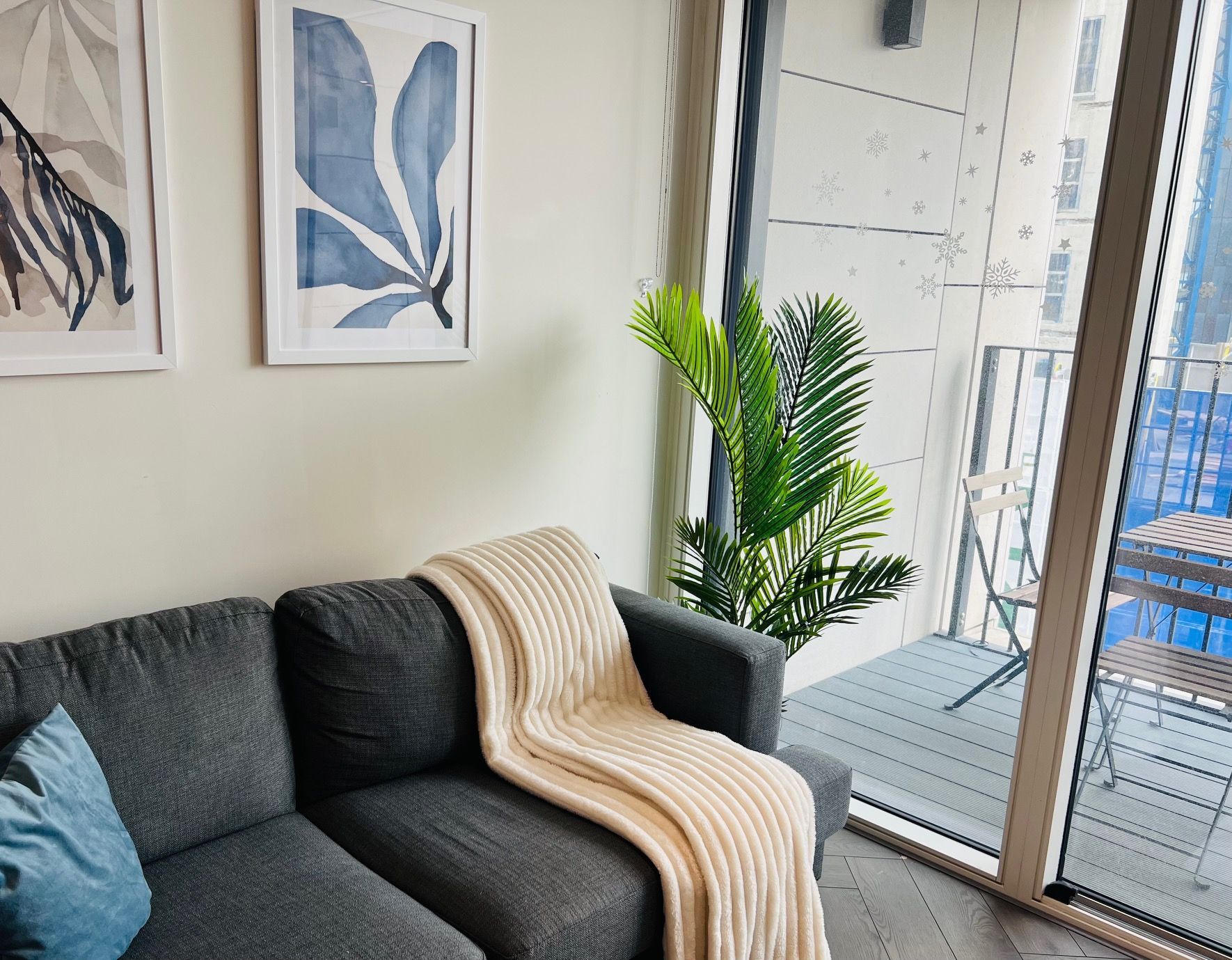 Gray sofa with throw blanket, blue art, and a balcony with a plant.