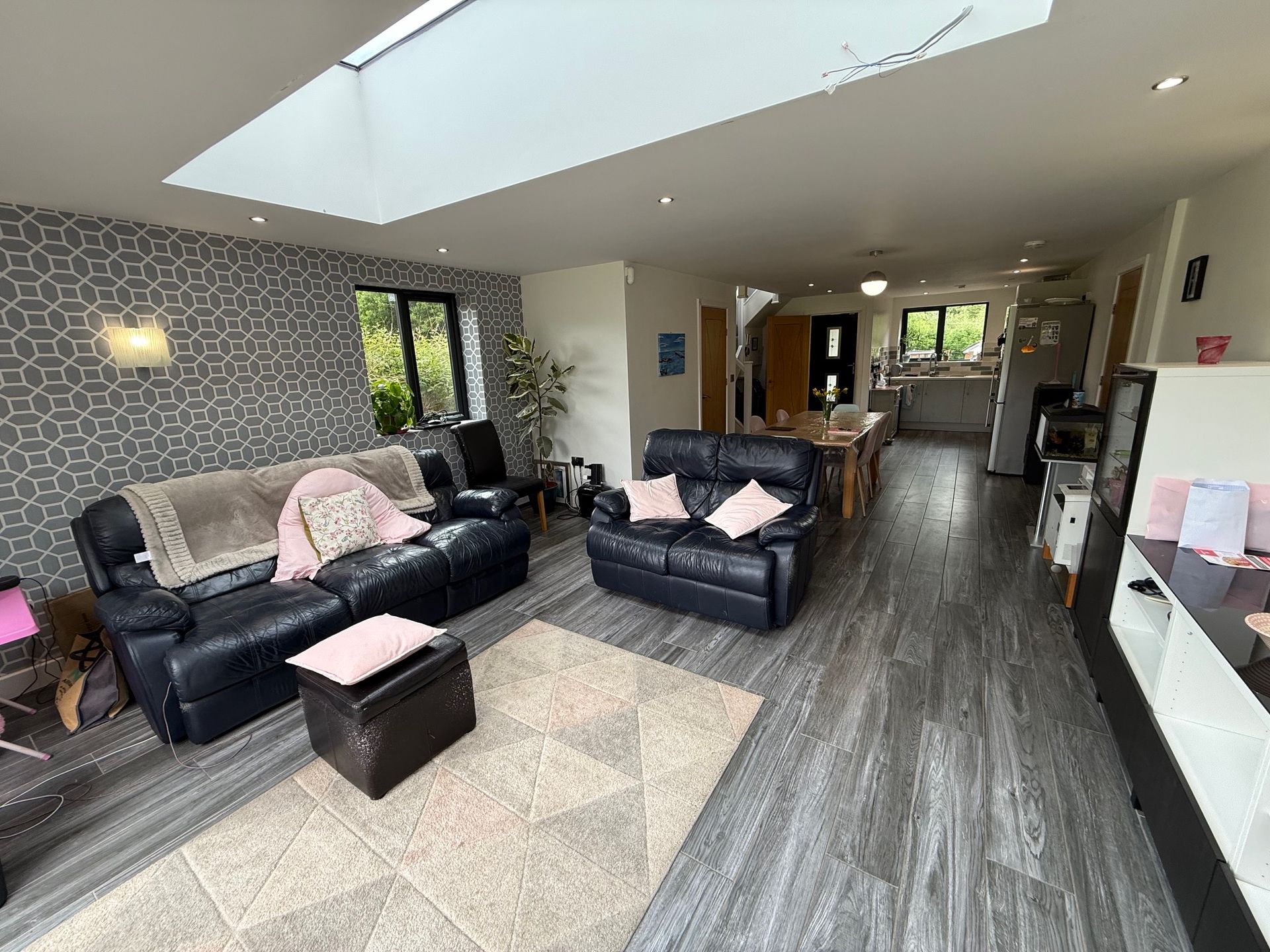 Living room with black leather sofas, geometric patterned wallpaper, and open to a dining area with a table.