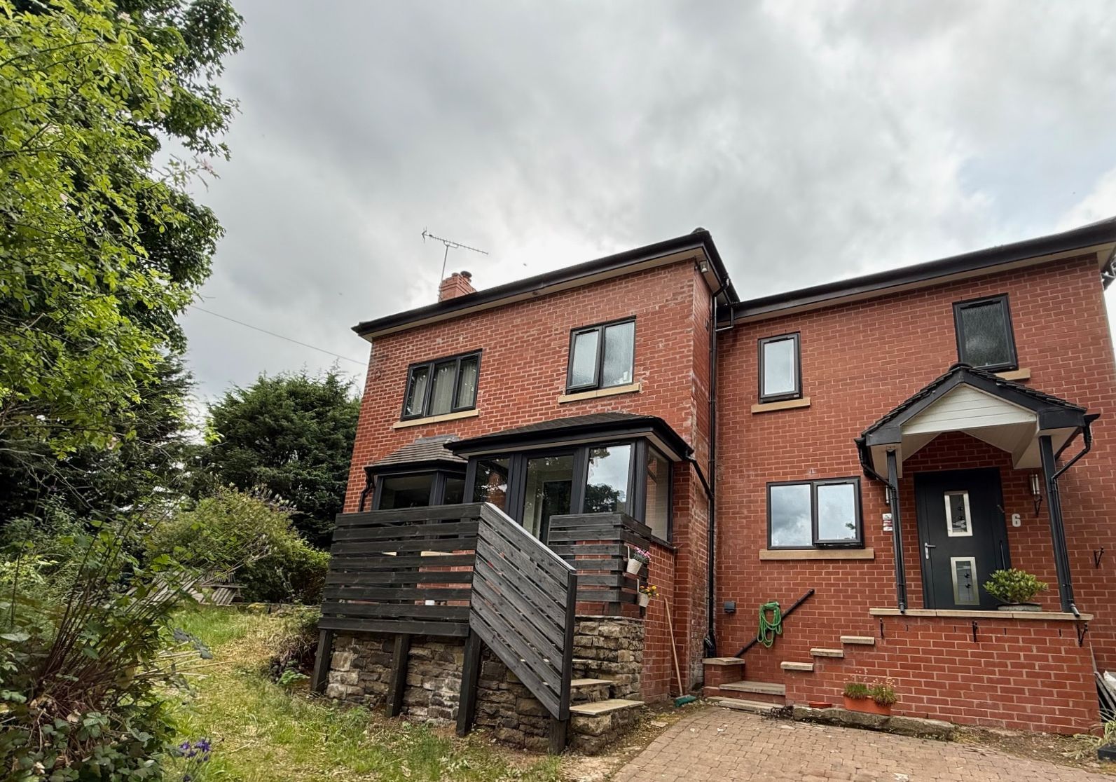 Two-story brick house with a porch and wooden deck, set against a cloudy sky.
