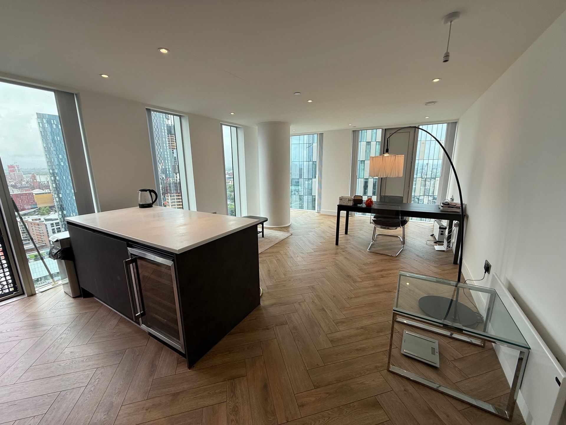 Modern open-plan kitchen and office area with large windows, island, desk, and arched floor lamp.