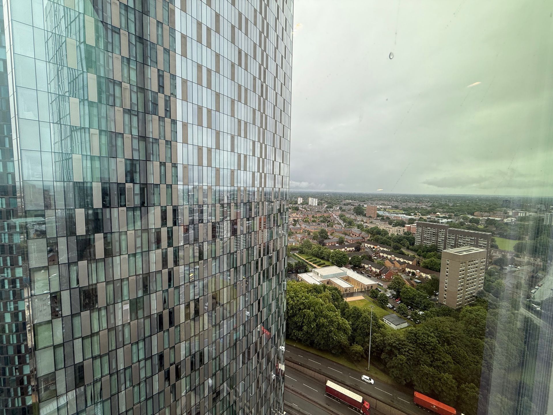 Modern skyscraper exterior next to a cityscape view, with cloudy sky.