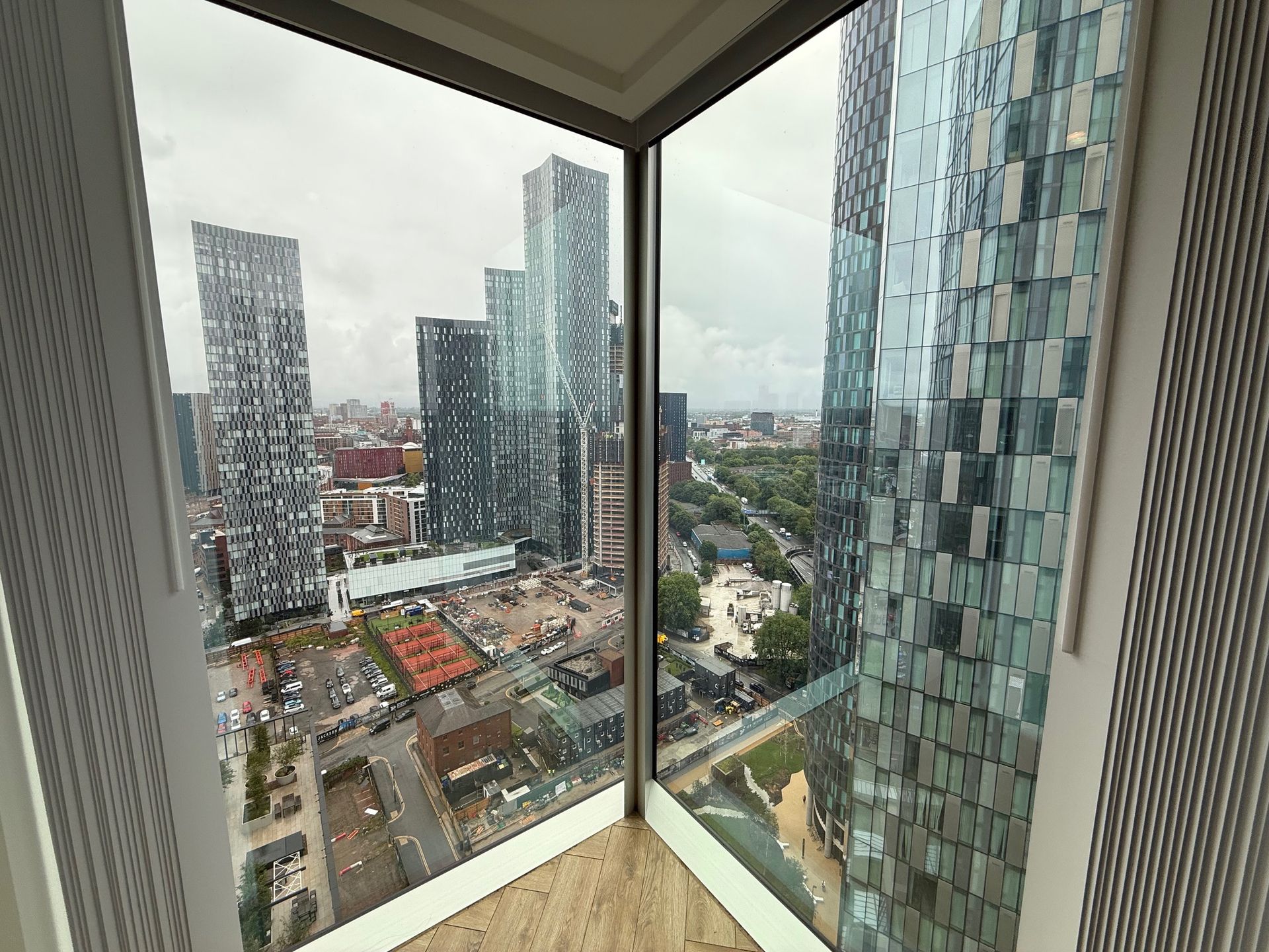 View from a tall building corner window of a city with skyscrapers, construction, and overcast sky.