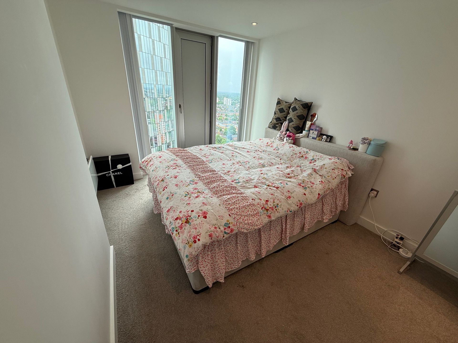 Bedroom with bed, floral bedding, window, and small cabinet.