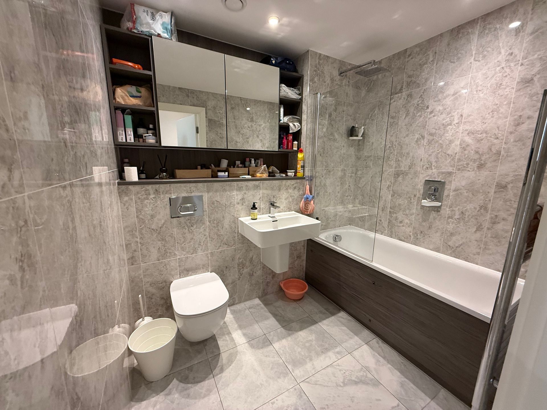 Modern bathroom with grey tile walls, white fixtures, and wooden accents.