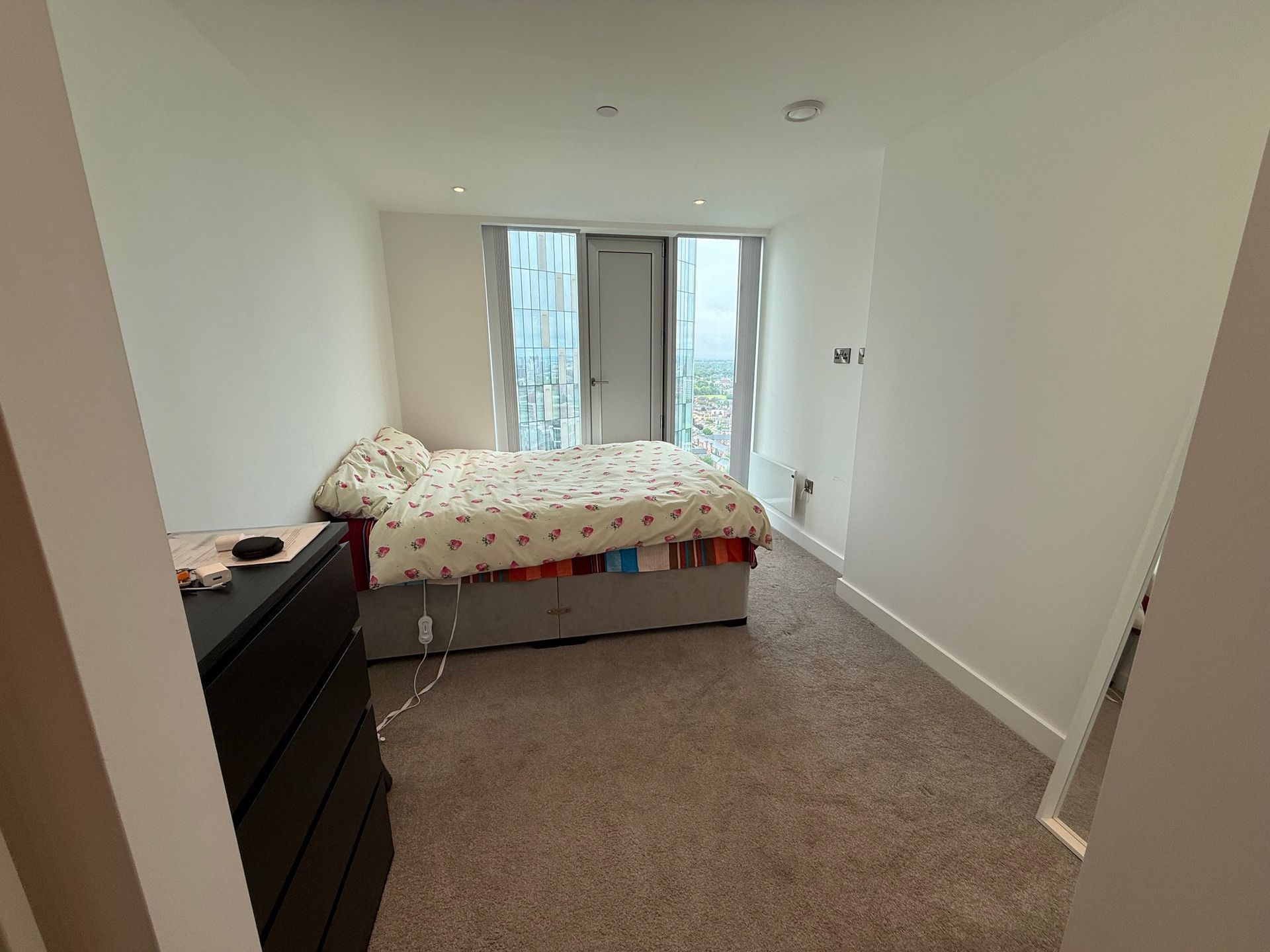 Bedroom with bed, dresser, carpet, and sliding glass doors to a balcony. White walls, natural light.