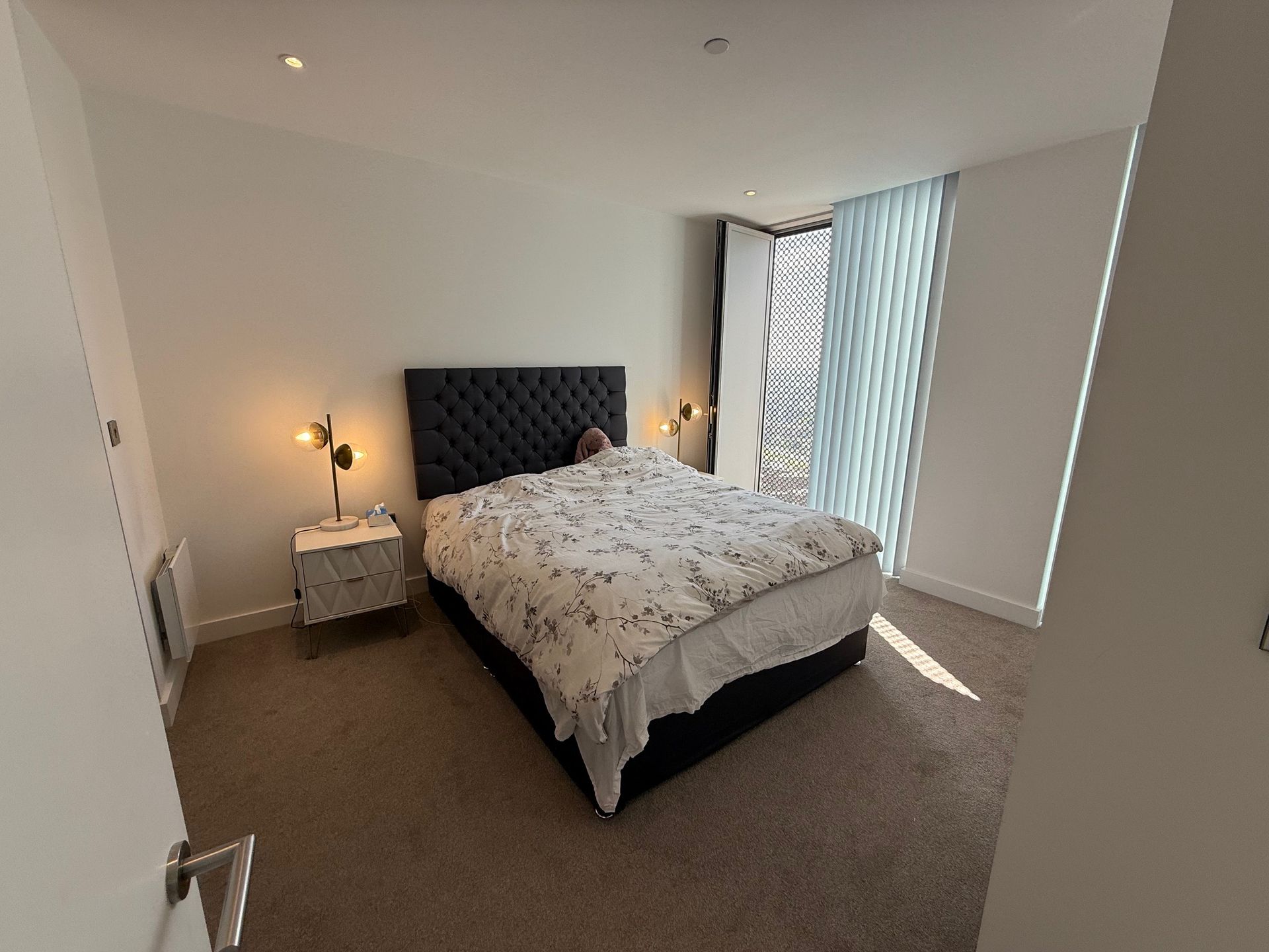 Bedroom with large bed, nightstands, and window with vertical blinds.