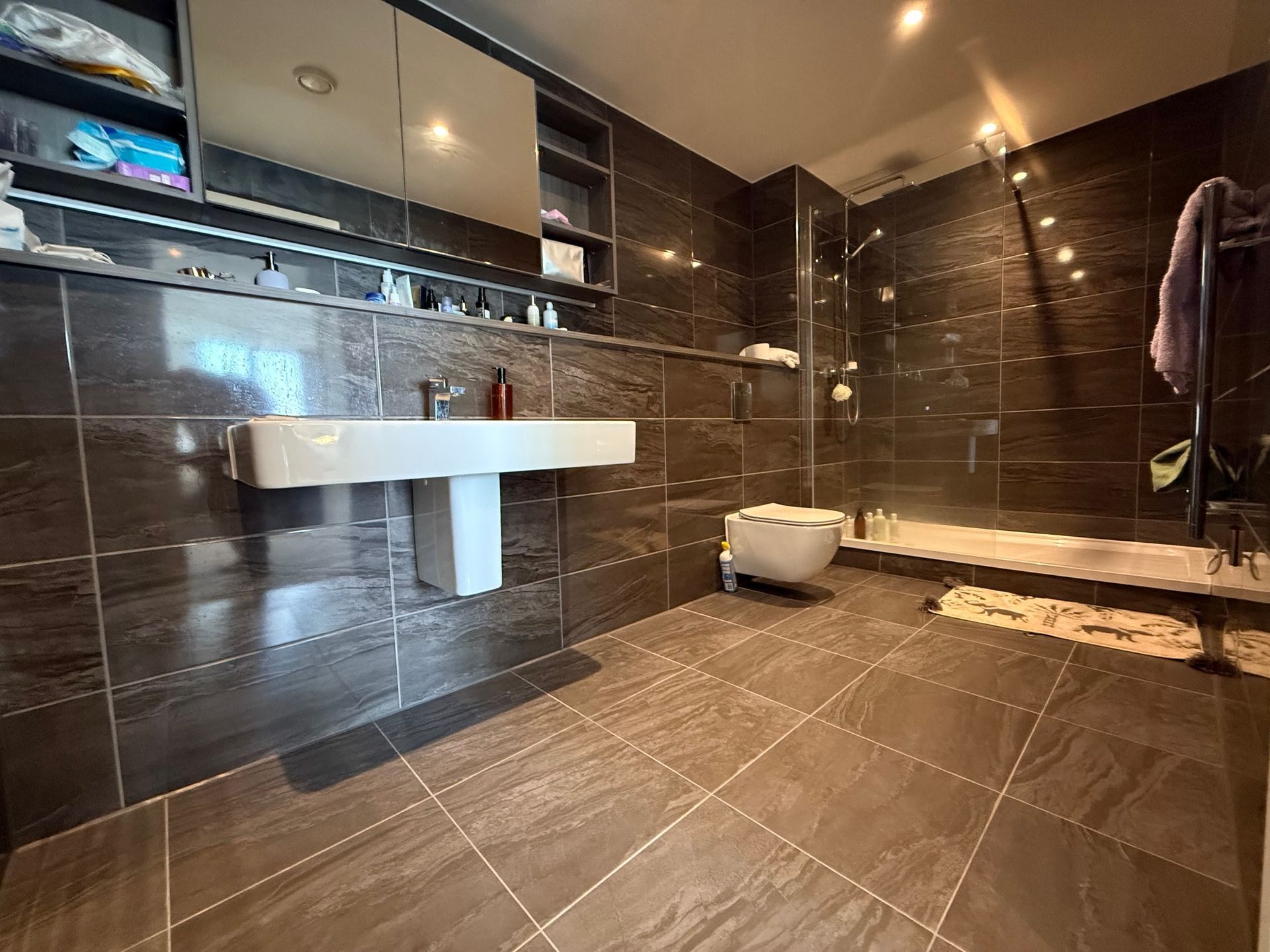 Modern bathroom with dark tile walls and floor, pedestal sink, shower, and toilet.