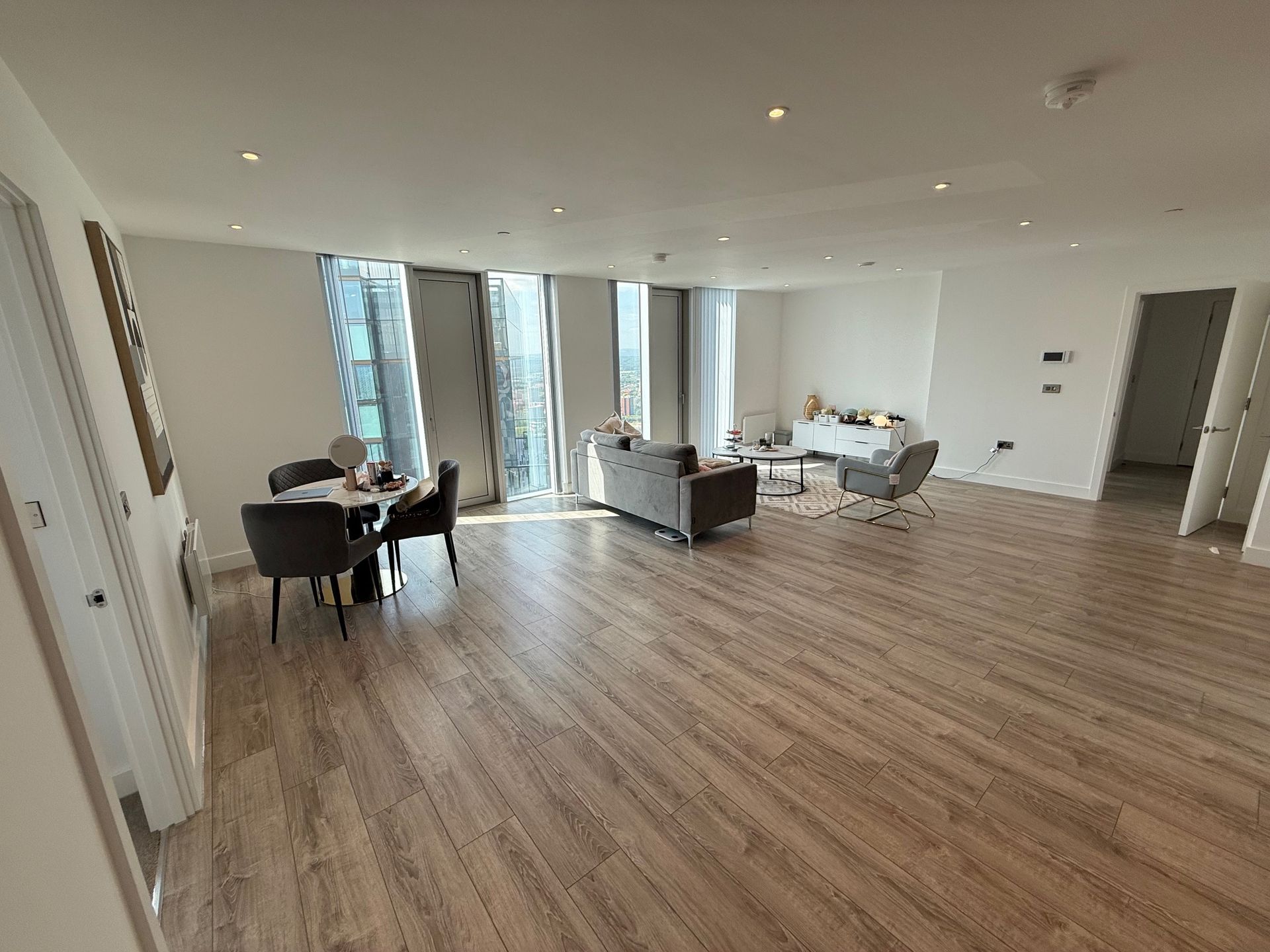 Spacious living room with wooden floors, dining table, sofa, and city view through large windows.