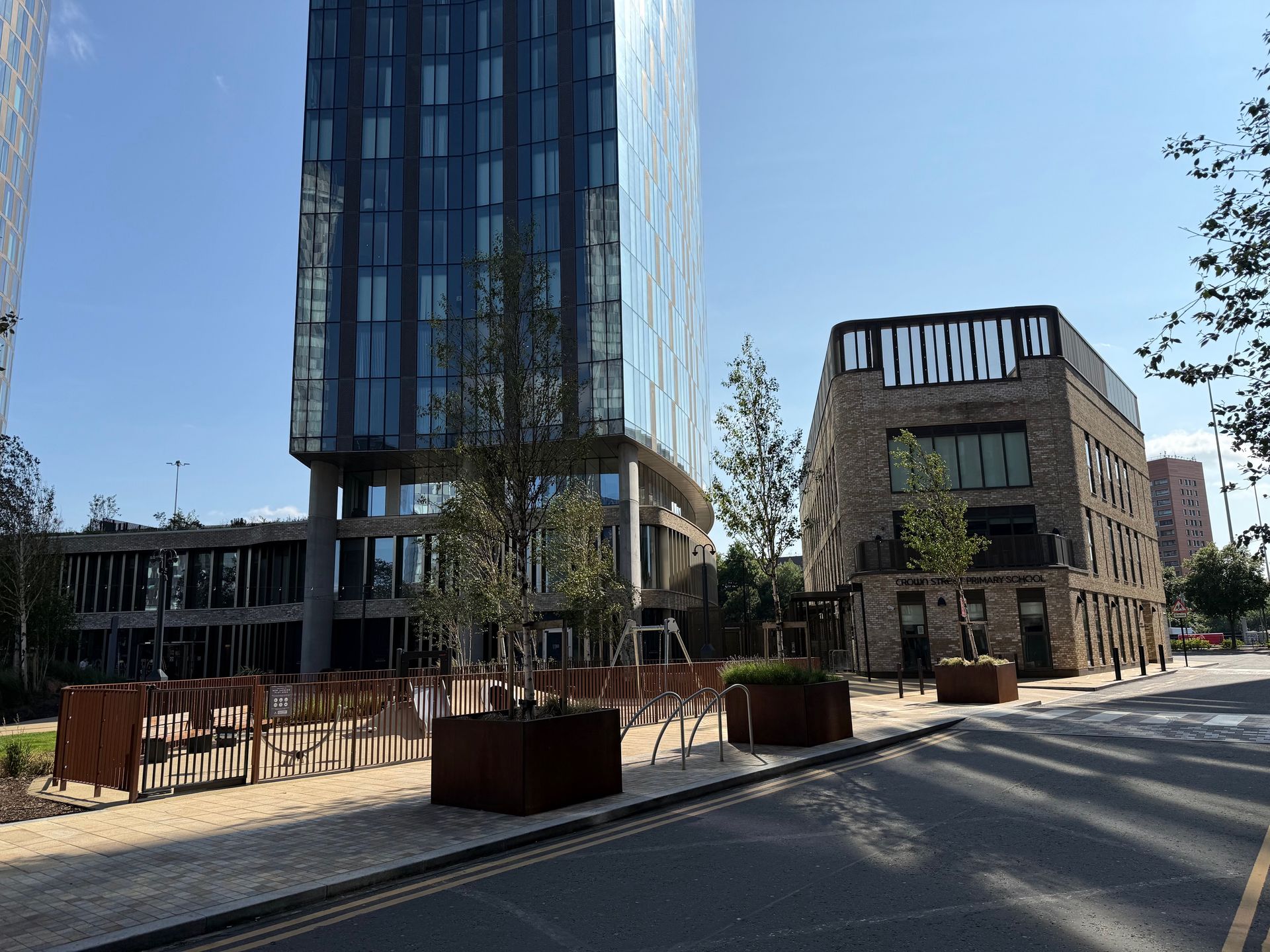 Modern buildings with trees, planters, and road, under a clear sky.