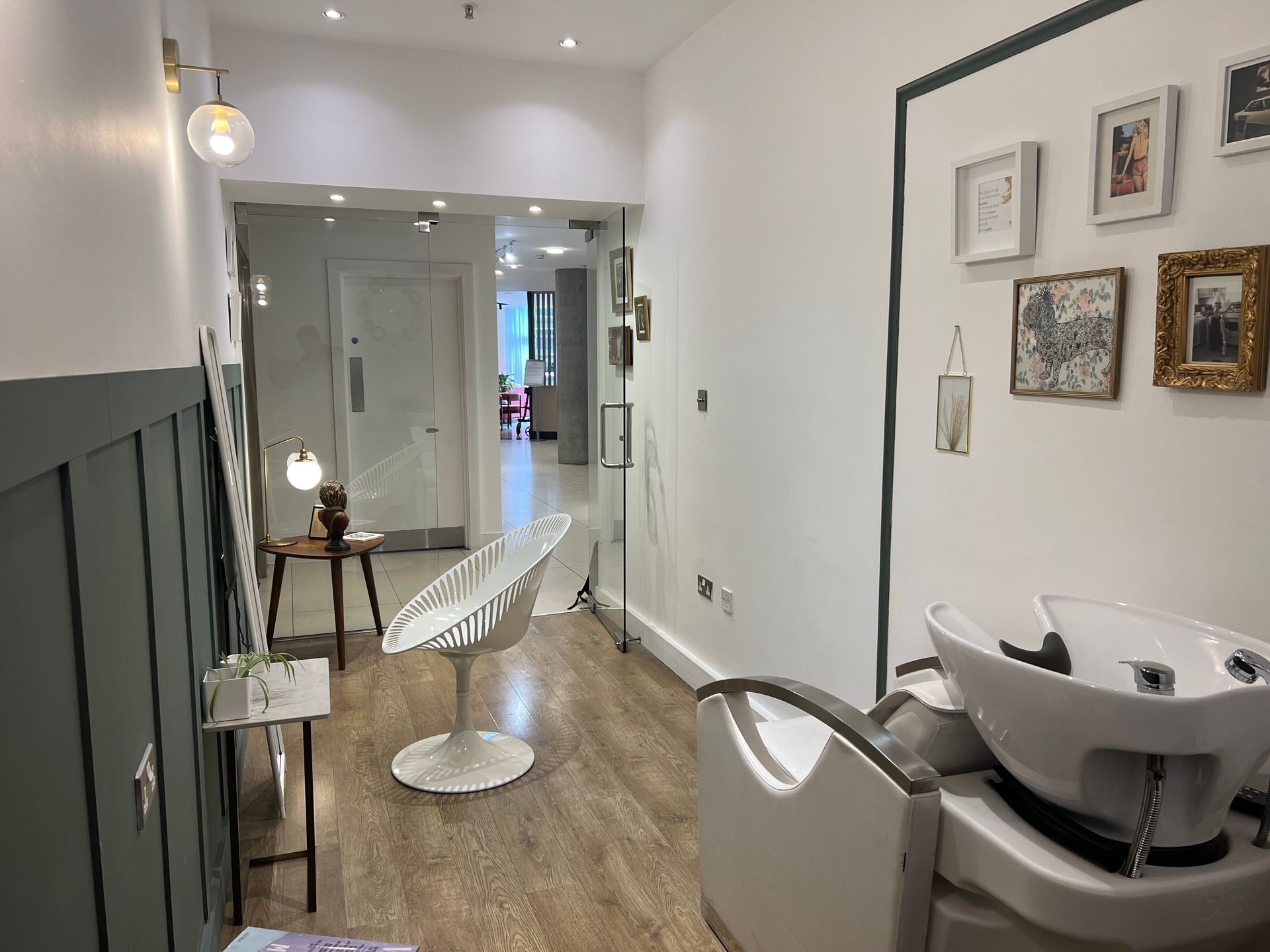 Salon interior with a white chair, a shampoo bowl, and framed artwork.