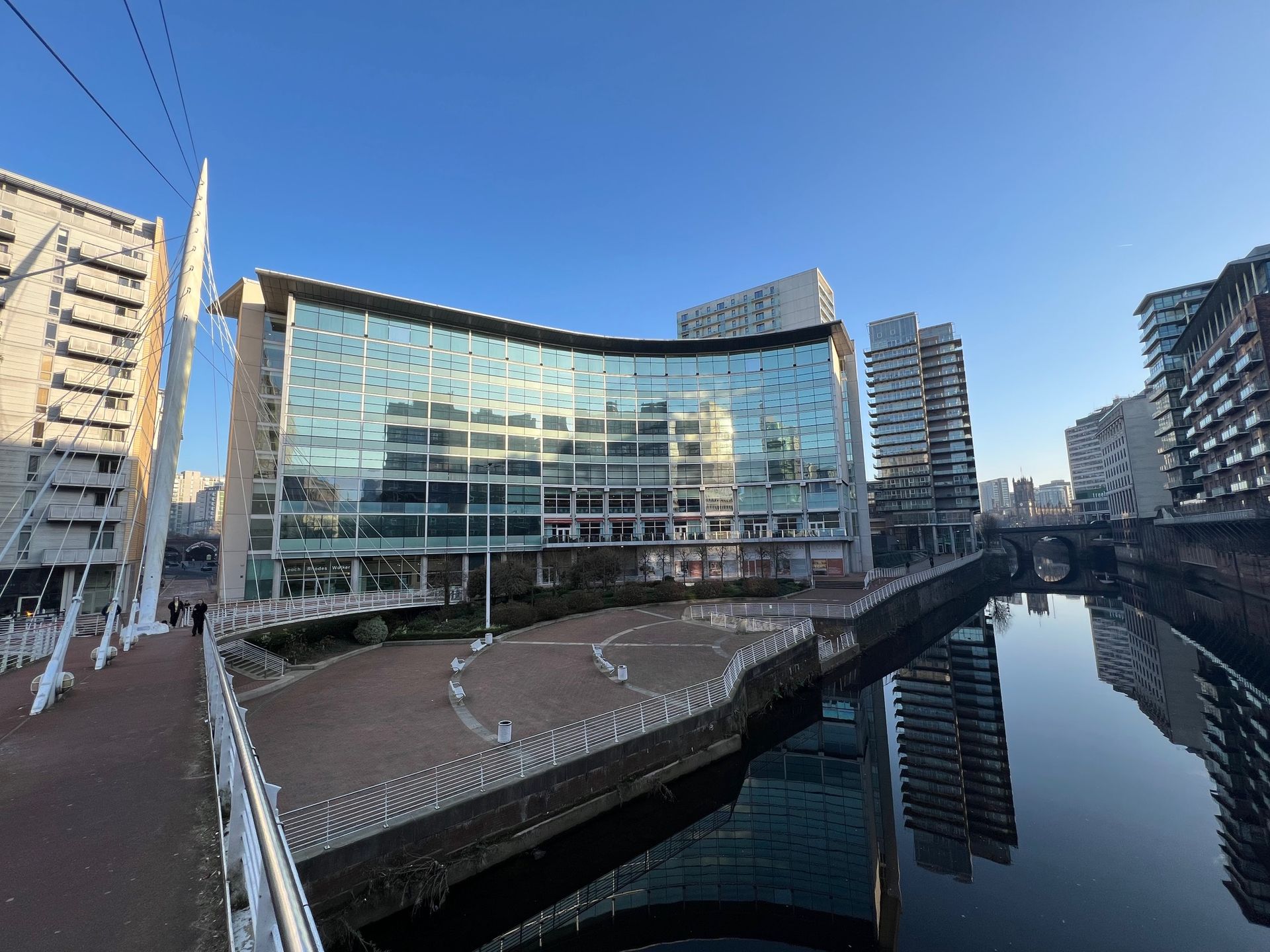 Modern building with curved glass facade on a canal under a clear blue sky.