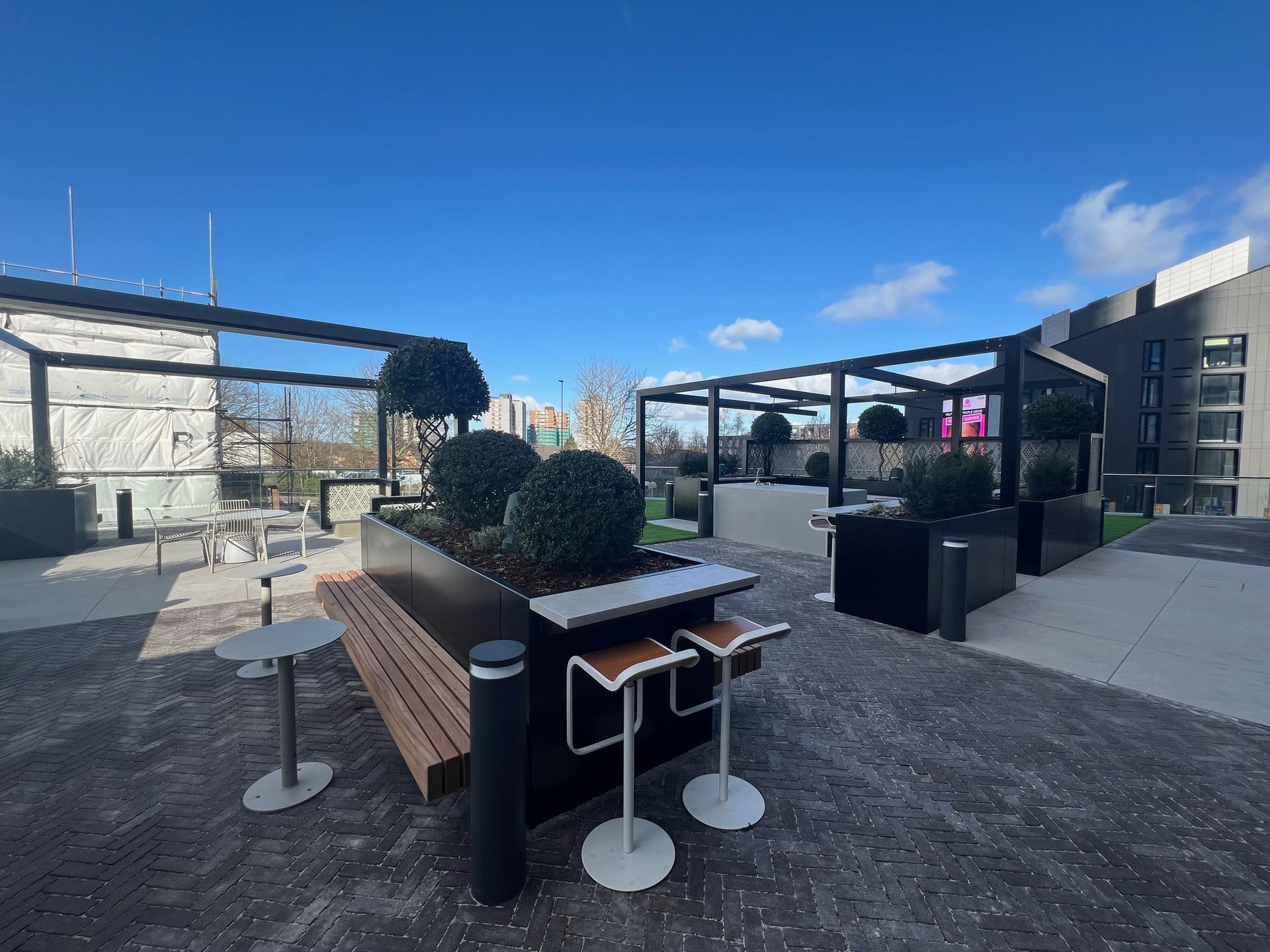 Rooftop patio with seating, planters, and a pergola under a blue sky.