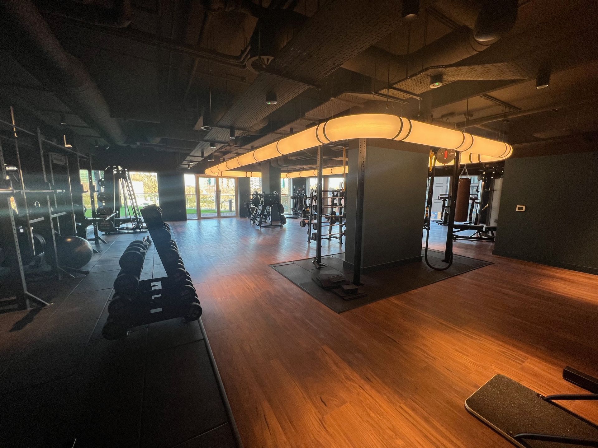 Gym interior with weight racks, exercise machines, and a large illuminated light fixture.