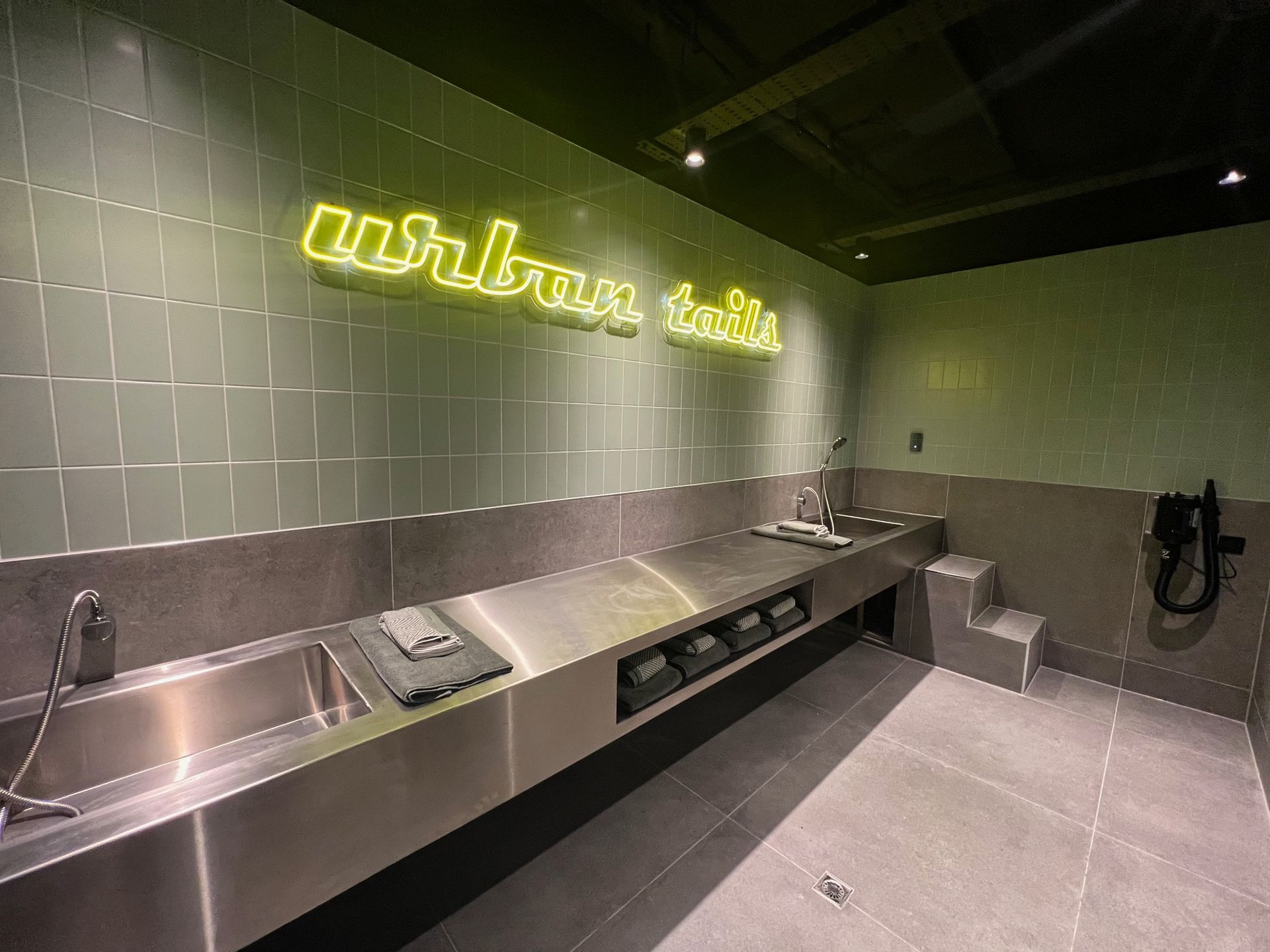 Dog washing station with stainless steel sinks, tiled walls, and neon