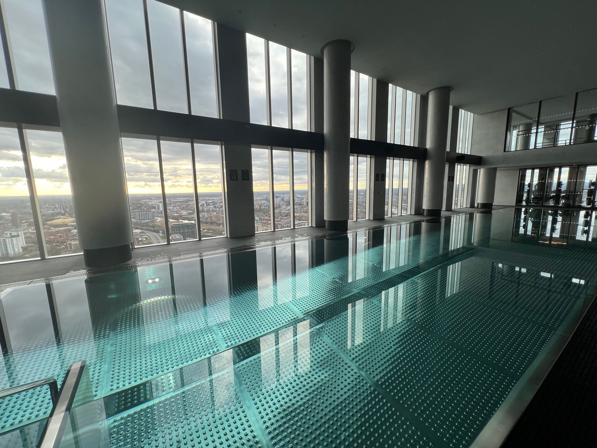 Indoor swimming pool with city view, large windows, and reflective water.