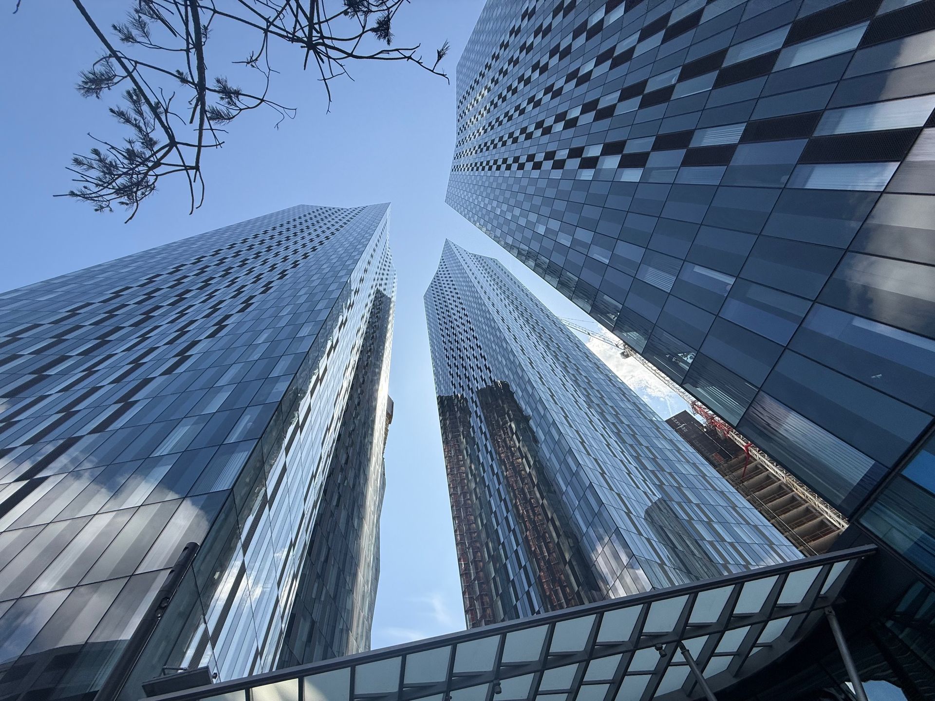 Low-angle view of three tall, modern skyscrapers with reflective glass facades against a blue sky.