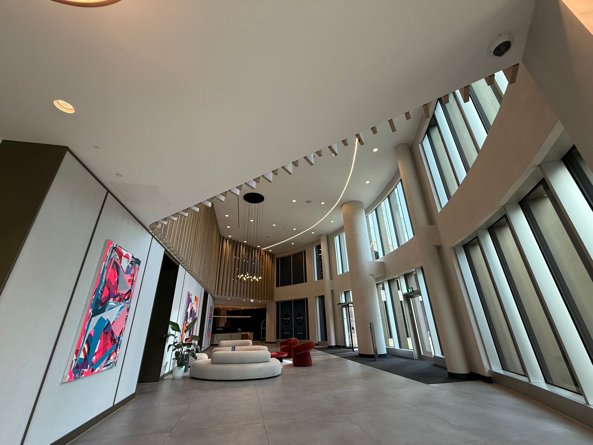 Lobby with large windows, modern art, and seating. Beige and white interior with curved ceiling and accent lighting.