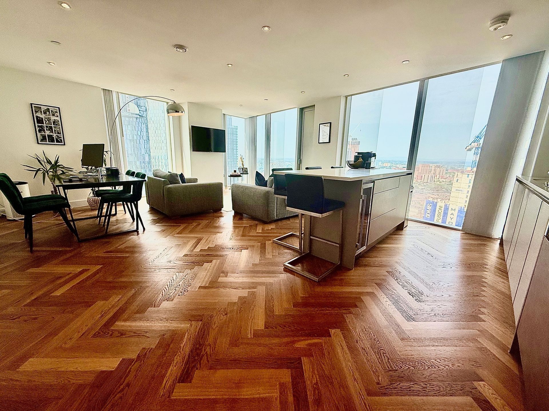 Spacious apartment interior with hardwood floors, dining area, kitchen island, and large windows offering a city view.