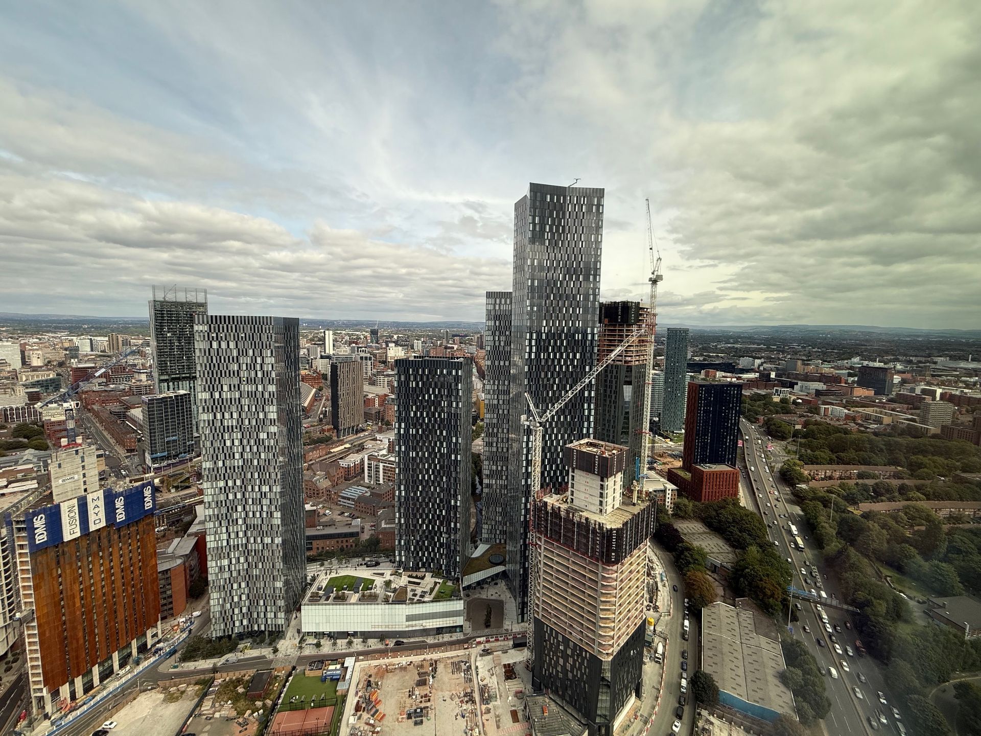 City skyline with high-rise buildings and construction crane under cloudy sky.