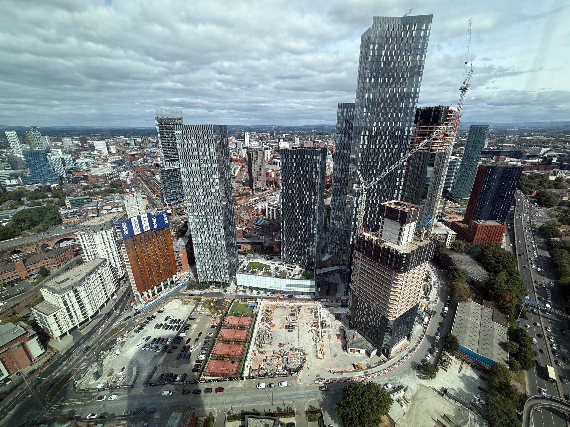 High-angle view of a city skyline with multiple skyscrapers under a cloudy sky. Construction site in foreground.