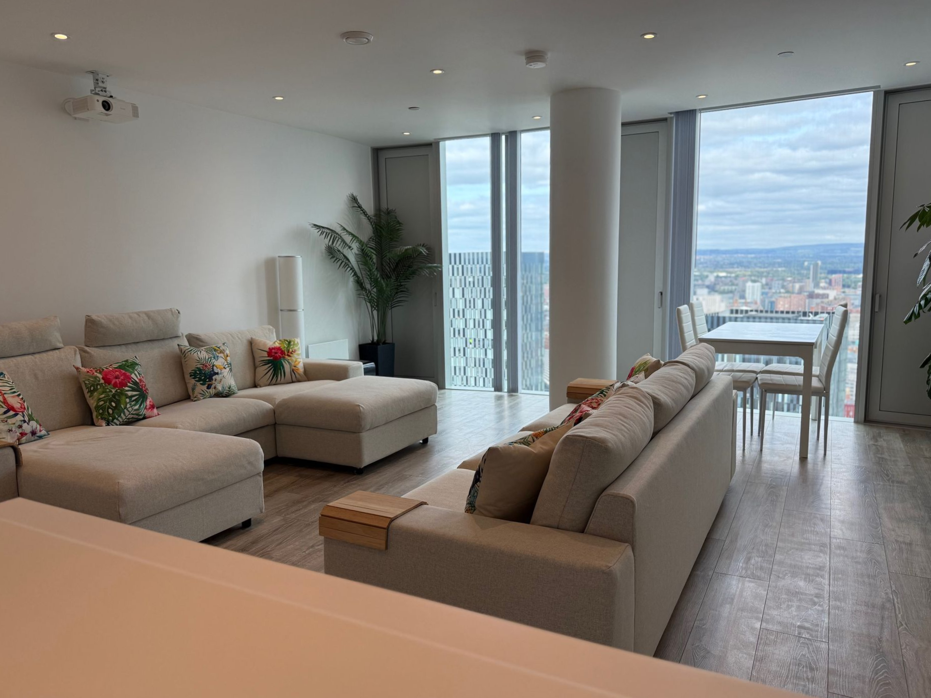 Modern living room with sectional sofa, dining area, and city view through large windows.