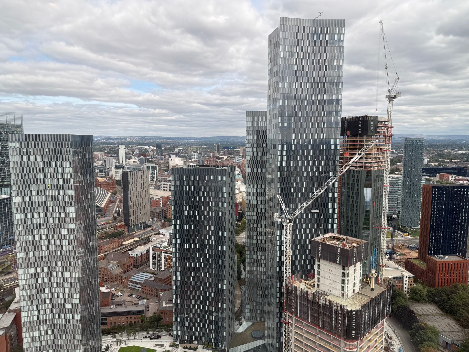 Skyscrapers in a city skyline under a cloudy sky, some under construction with cranes.