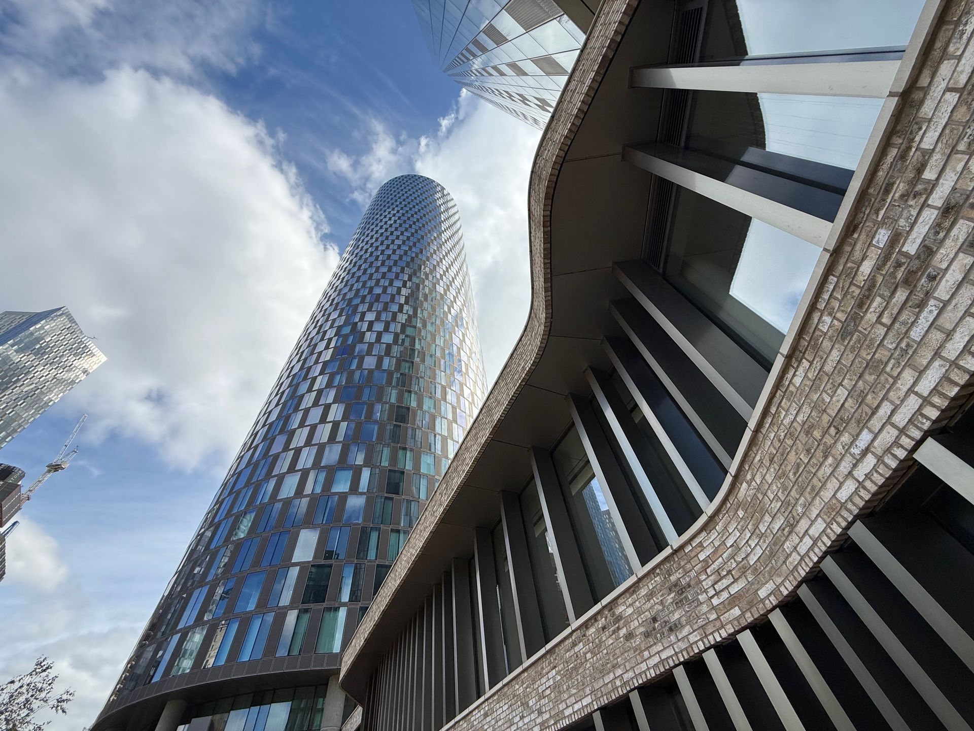 Skyscrapers against a cloudy sky, shot from a low angle. Brick facade in the foreground, glass tower in the center.