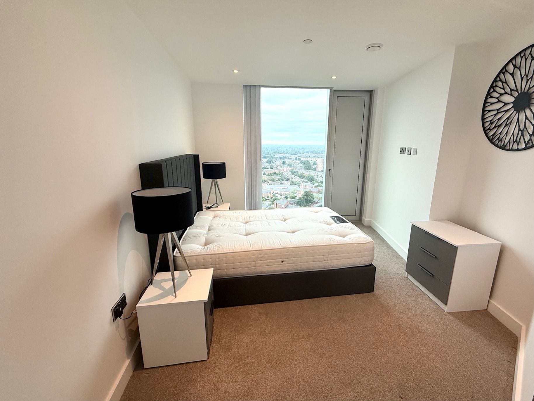 Bedroom with bed, bedside tables, lamps, and a view through a large window.