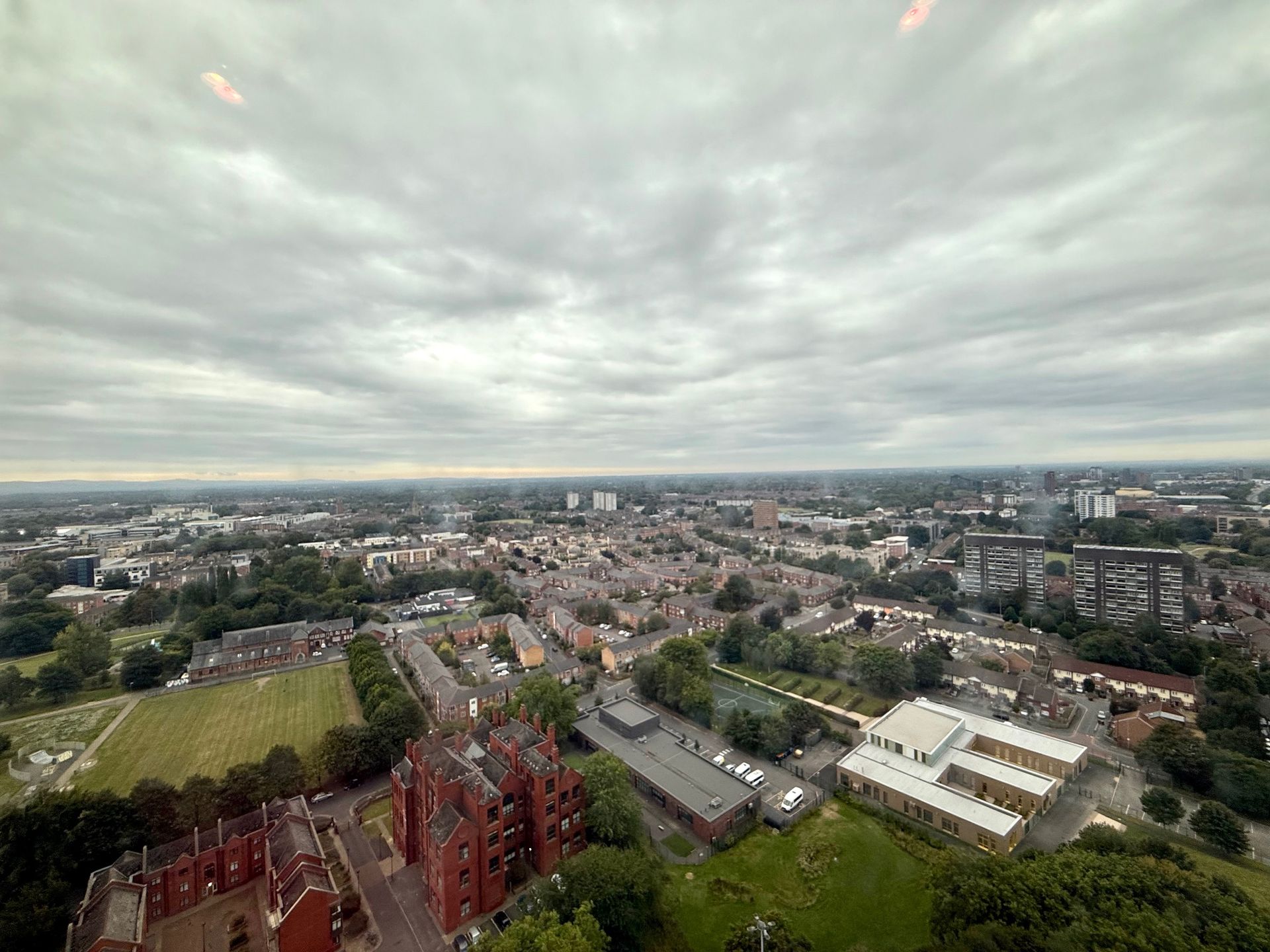 Aerial view of a town under a cloudy sky. Buildings, trees, and roads fill the landscape.