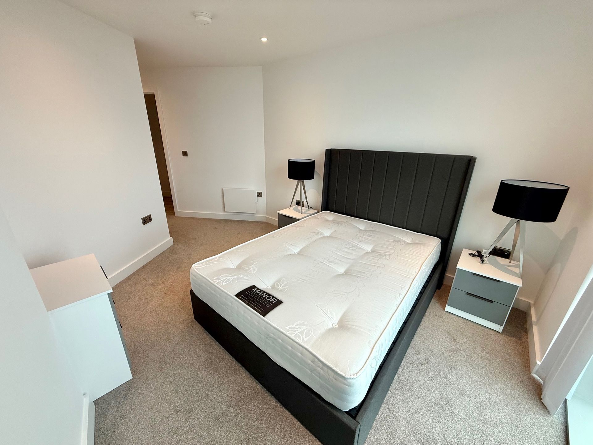 Bedroom with bed, nightstands, lamps, and a chest of drawers. Carpeted floor and white walls.