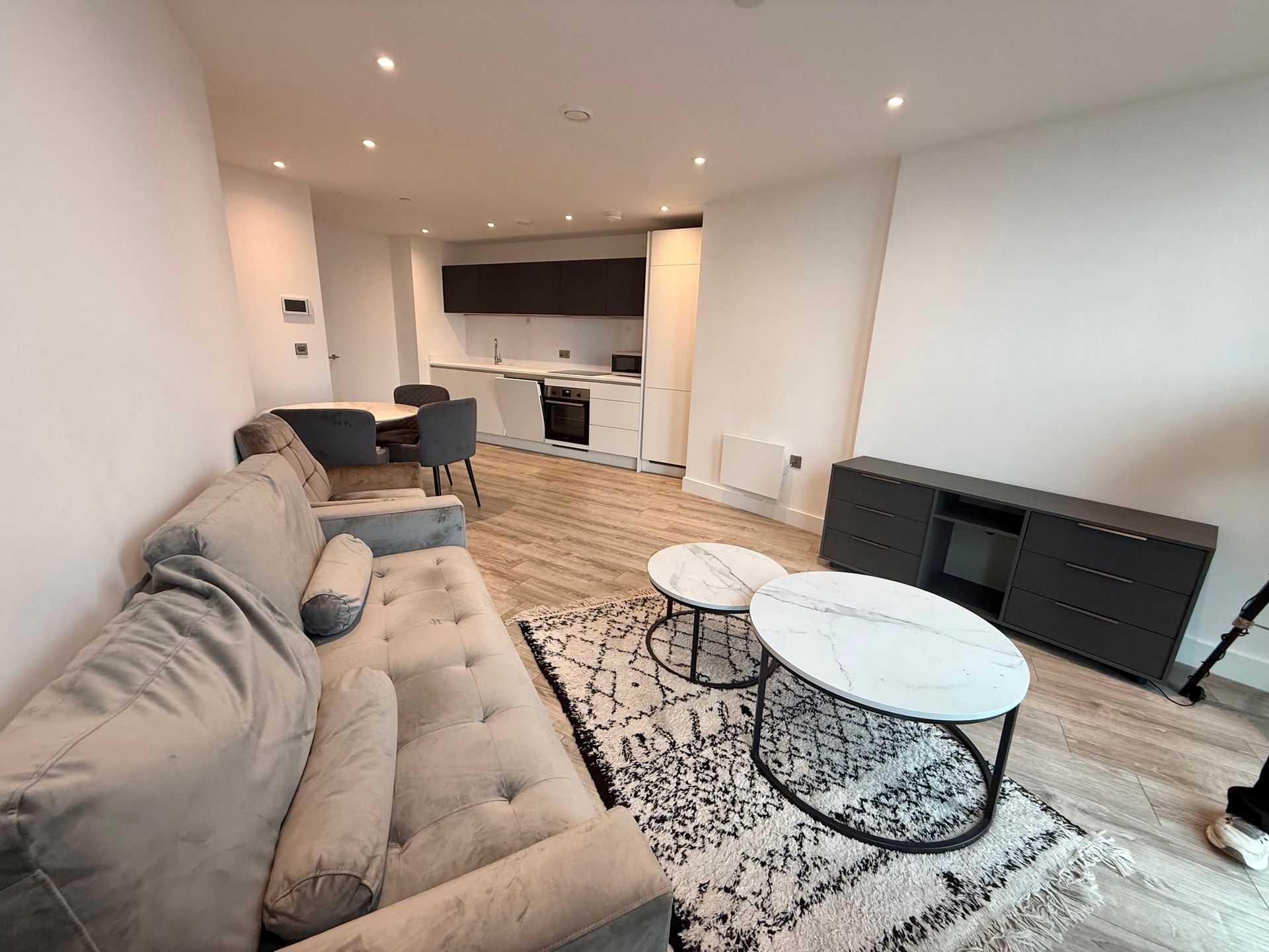 Living room with sofa, coffee tables, dining set, and dark cabinets against white walls and light wood floors.