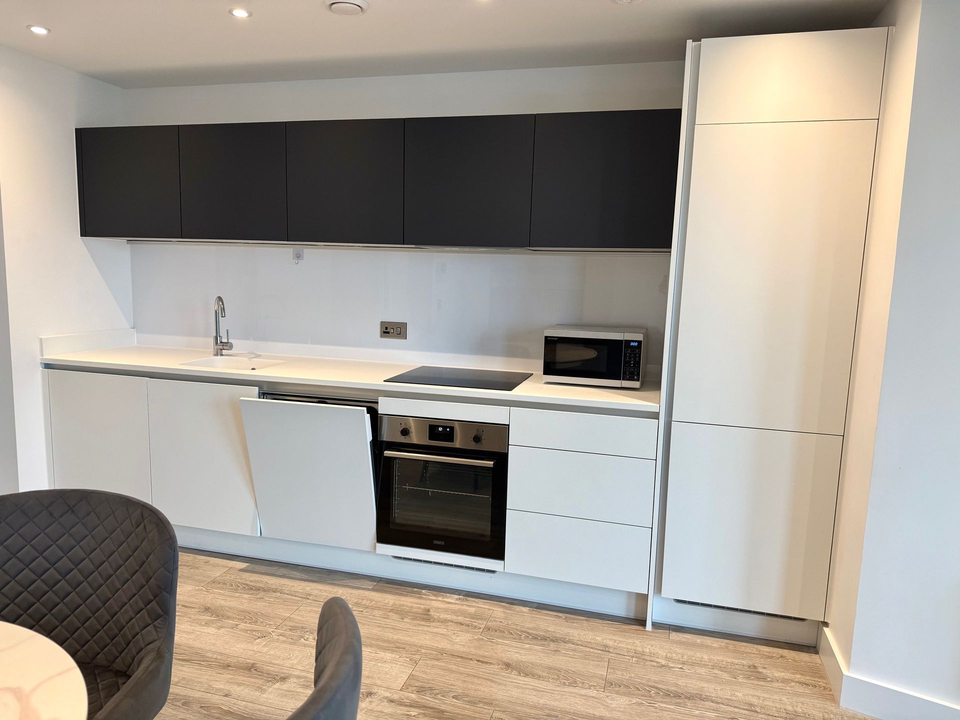 Modern kitchen with white and dark gray cabinets, a built-in oven, and a microwave.