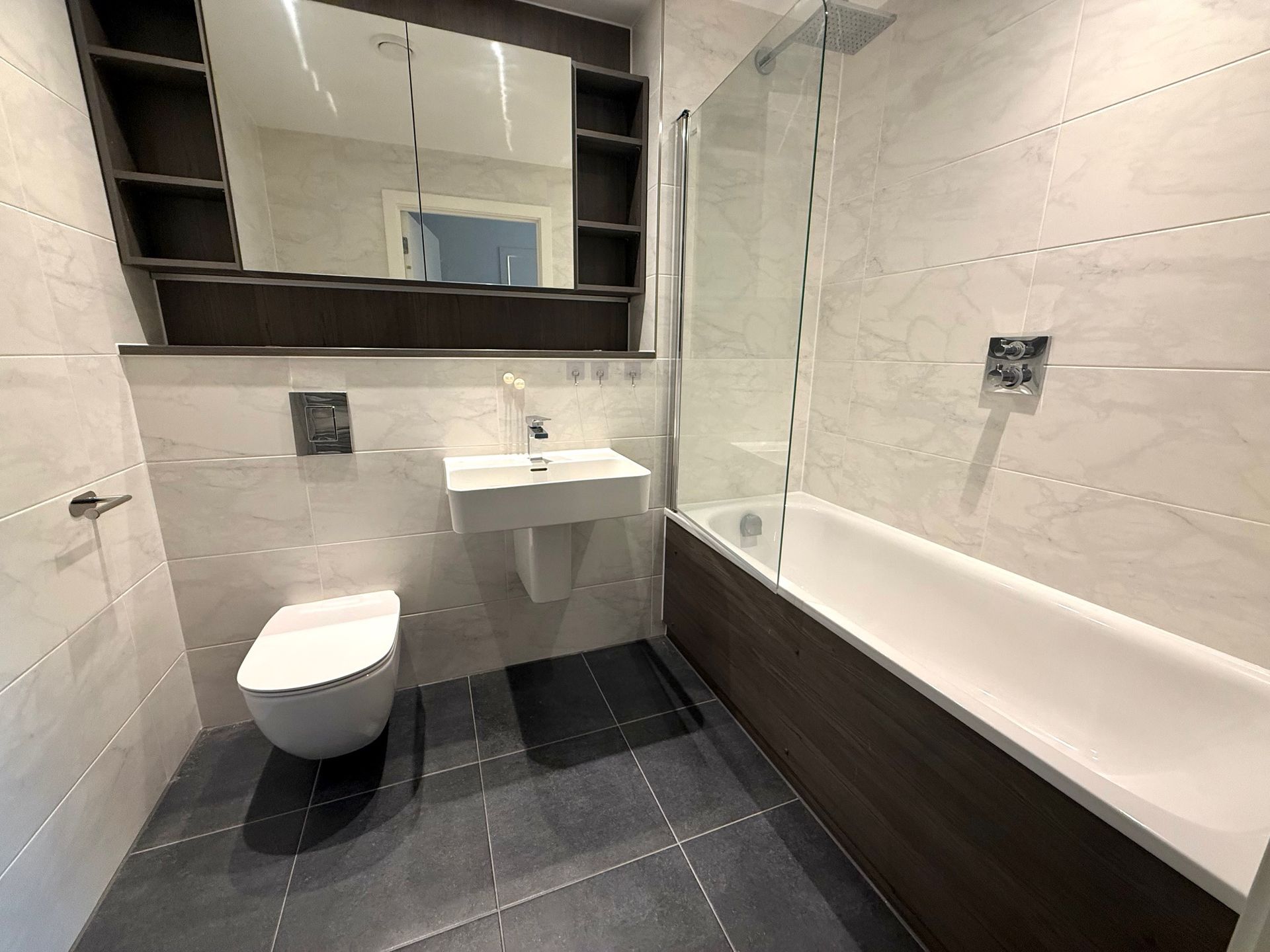 Modern bathroom with white walls, dark wood accents, toilet, sink, and bathtub.