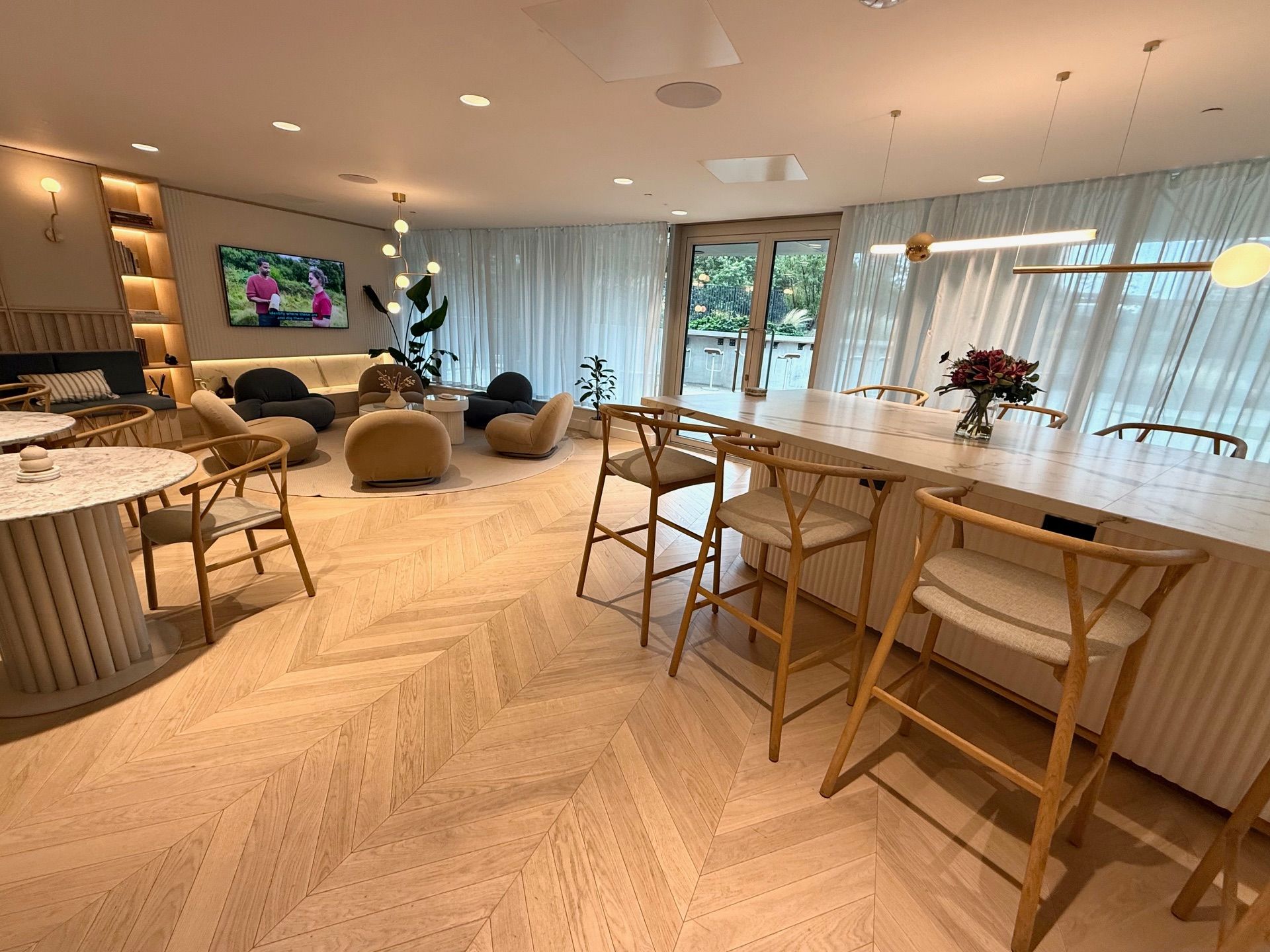 Bright, modern lounge with light wood floors, bar seating, and comfortable chairs. Large windows look out to greenery.