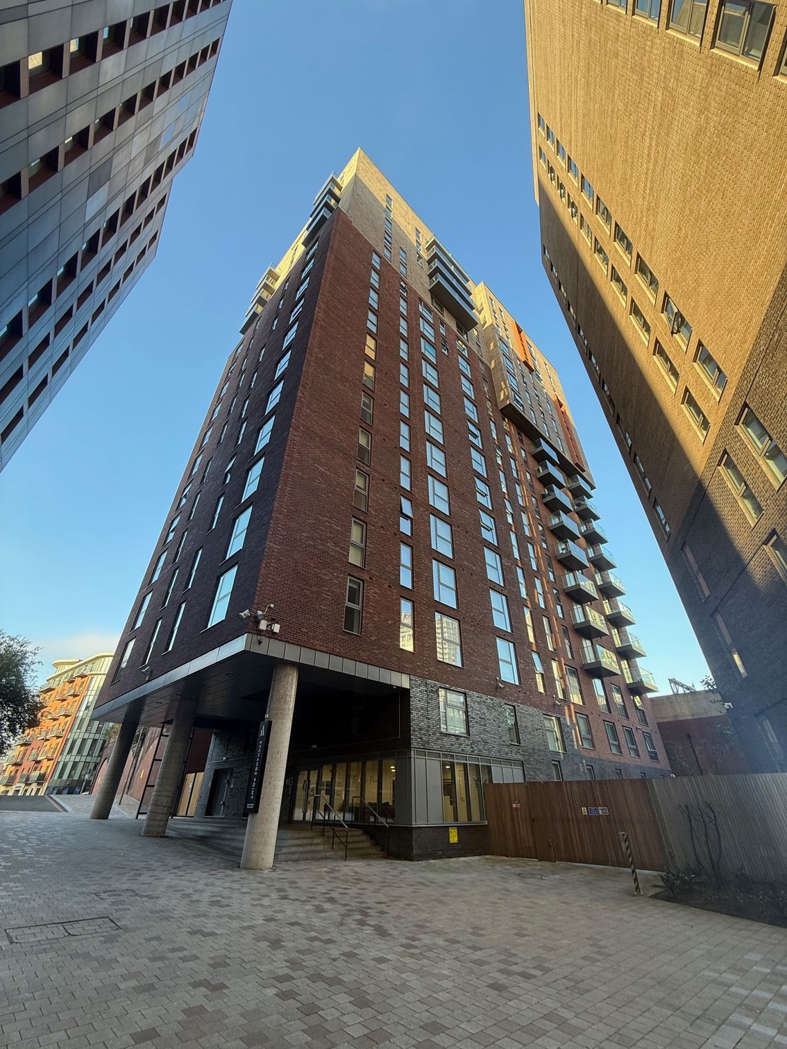 Tall brick apartment building with several windows, against a blue sky, flanked by other buildings.