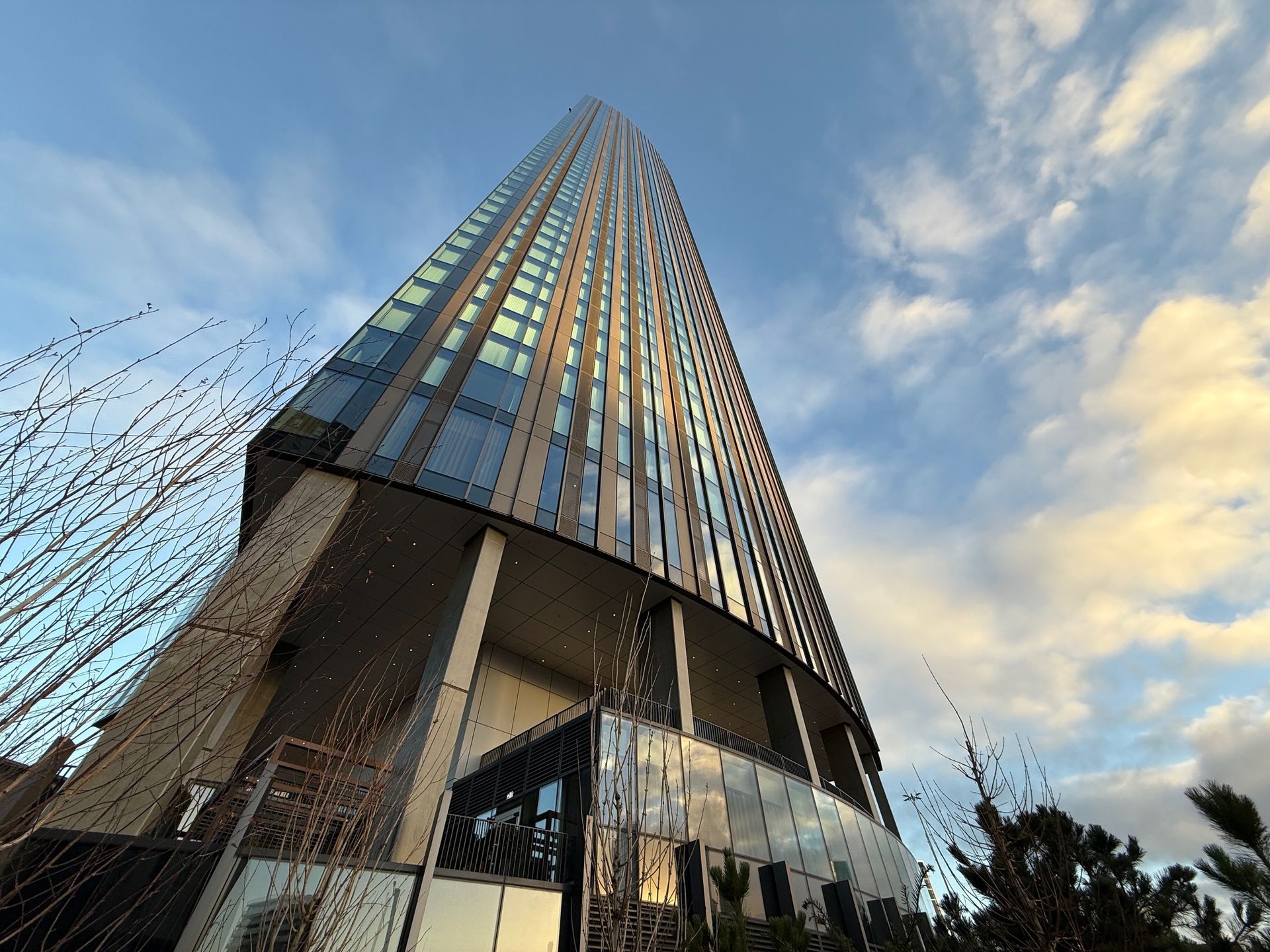 Modern skyscraper viewed from below, against a cloudy blue sky.