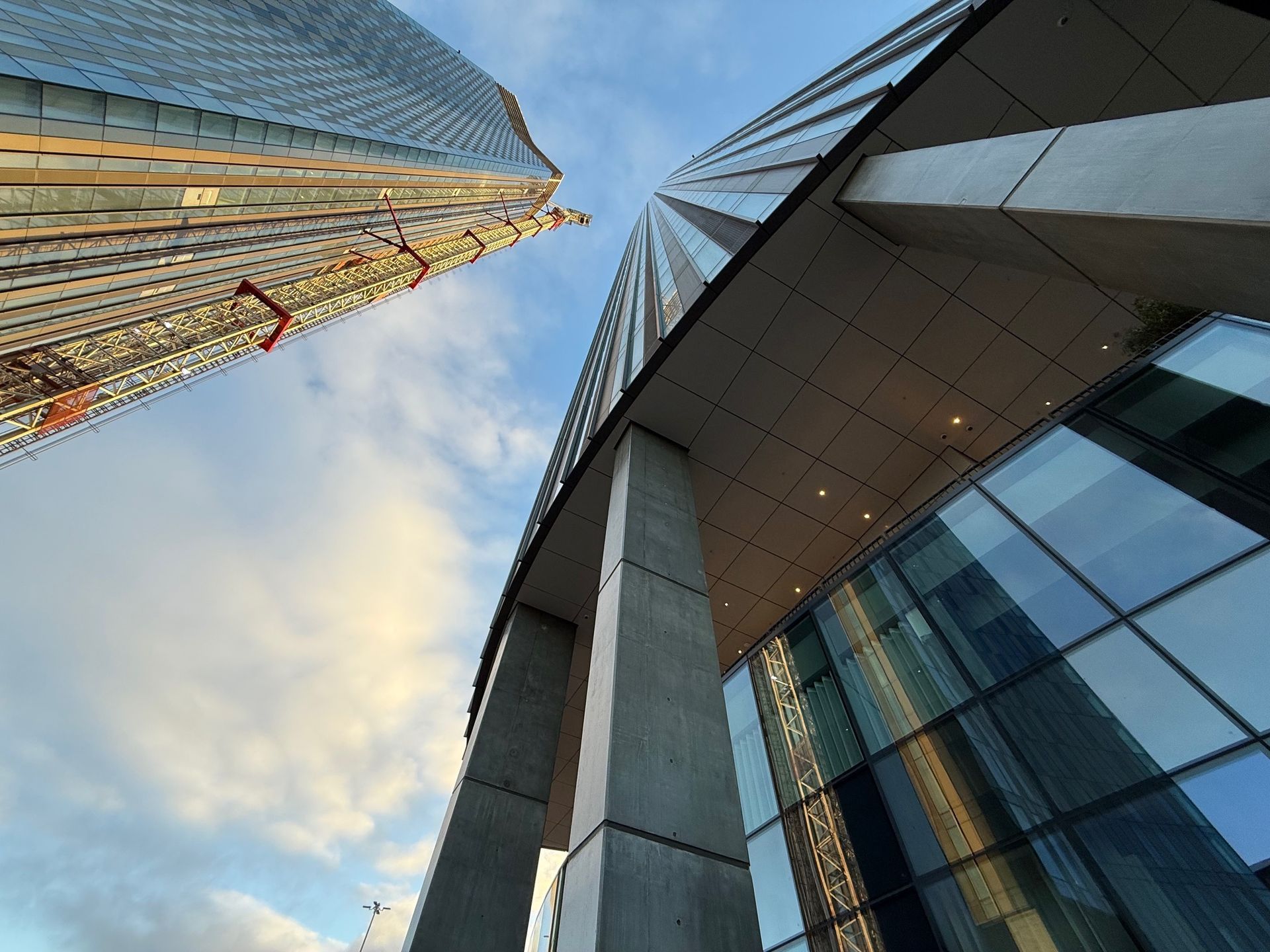 Low-angle view of two skyscrapers against a cloudy sky. One has visible scaffolding.