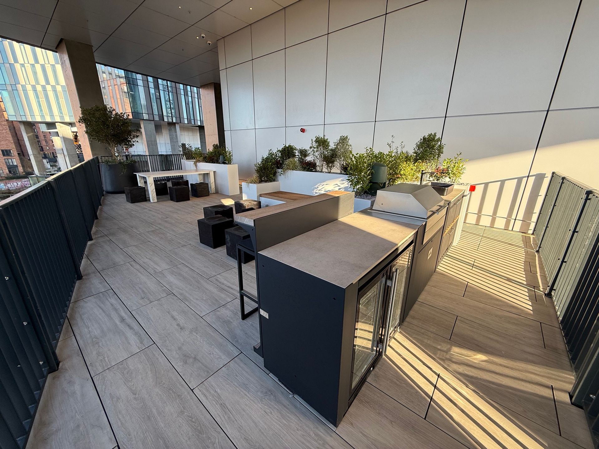 Rooftop deck with outdoor kitchen, grill, and seating. City buildings visible in the background.